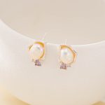 Baroque pearl stud earrings with small purple amethyst accents on a display bust