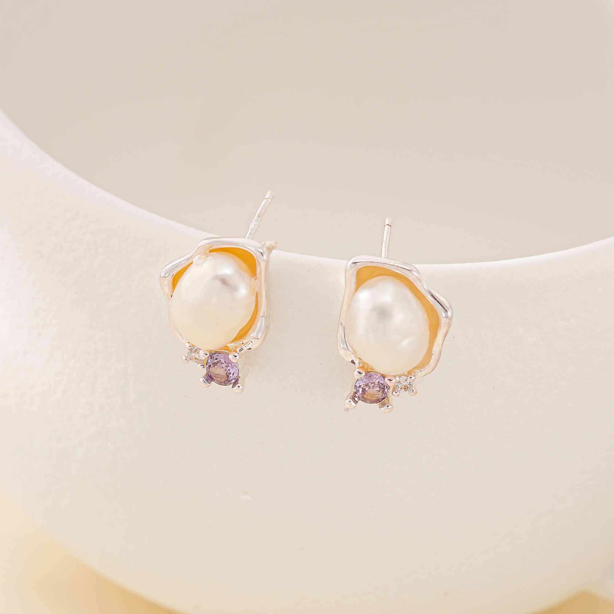 Baroque pearl stud earrings with small purple amethyst accents on a display bust