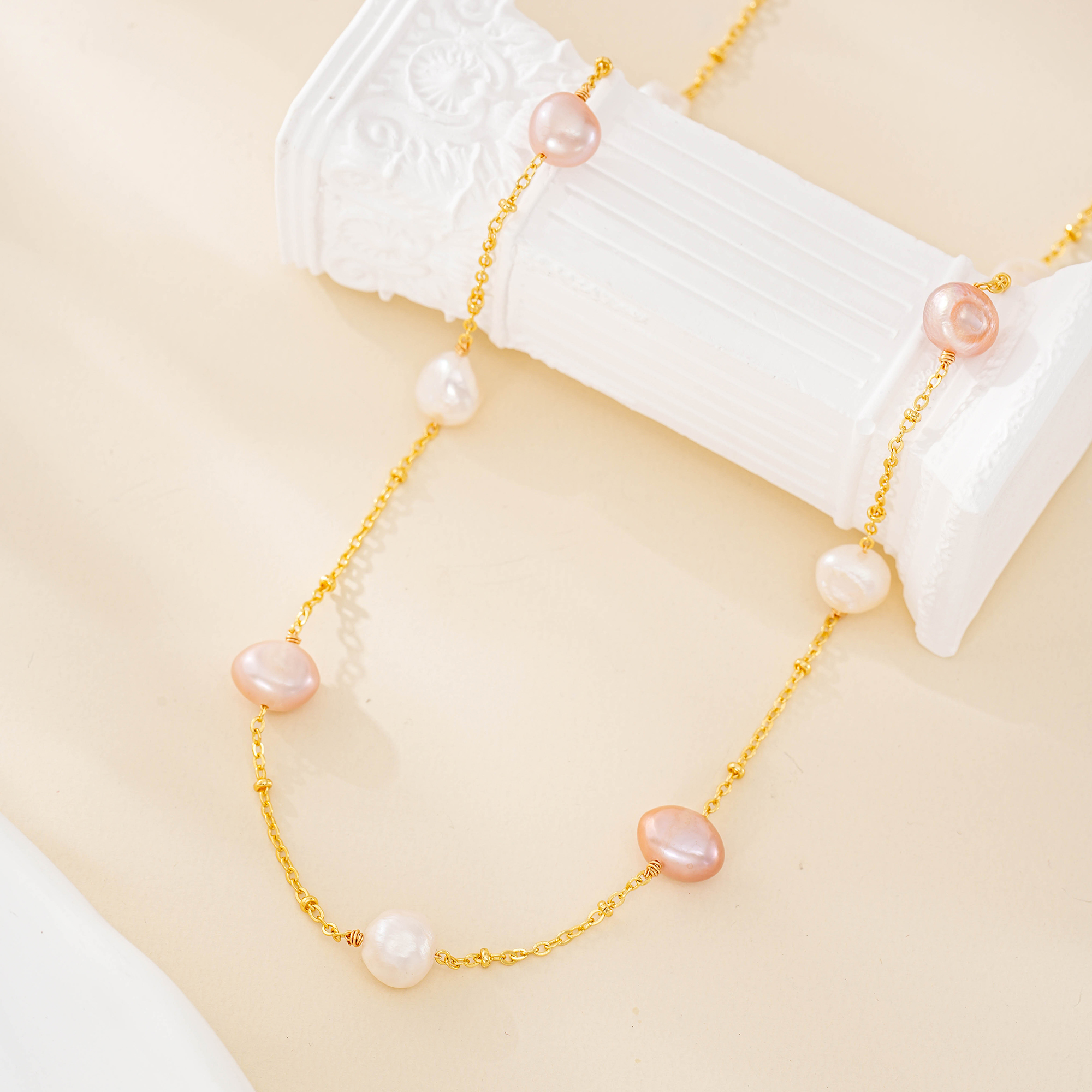 Close view of pink and white pearls spaced along a gold-tone necklace chain