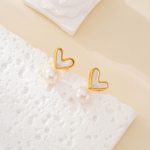 Heart-shaped shell and pearl drop earrings laid flat on a white textured surface
