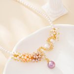 Close view of cream, peach and lilac pearl clusters with purple pearl drop on a necklace