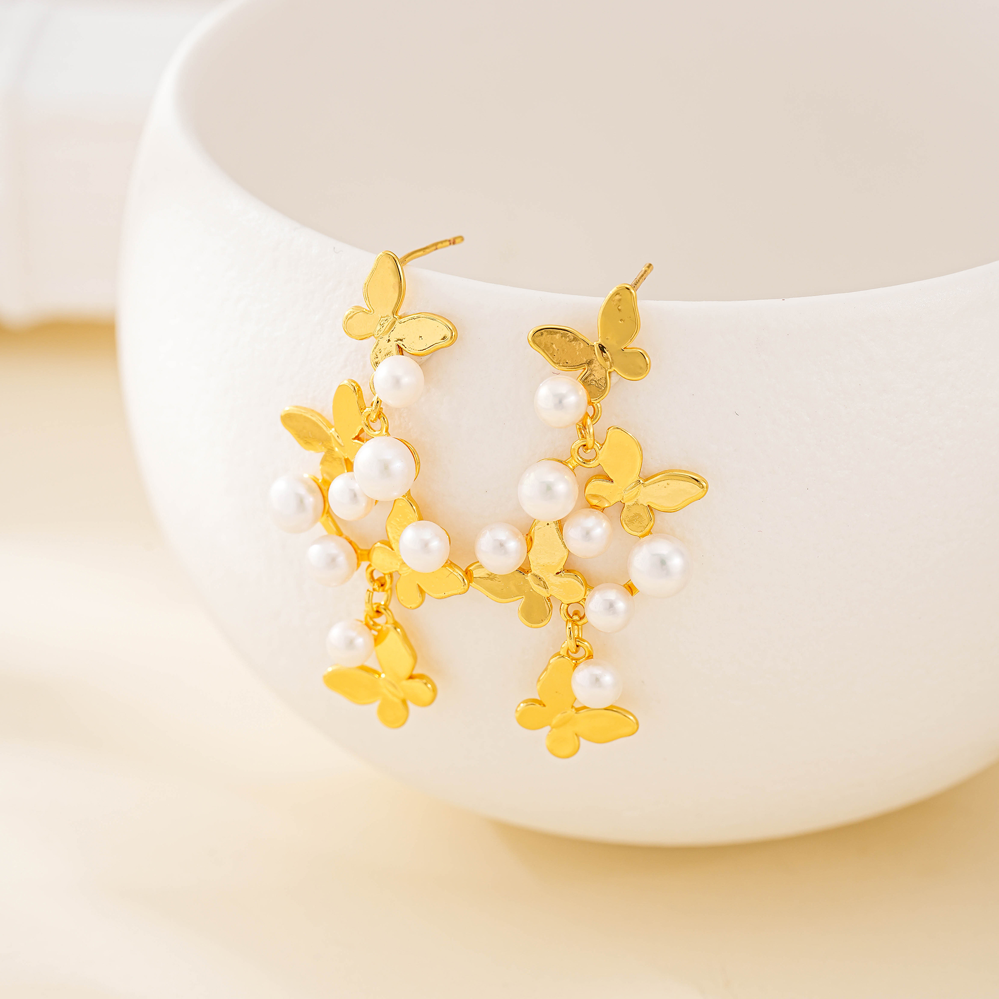 Butterfly and freshwater pearl earrings with gold-tone stud posts on white display