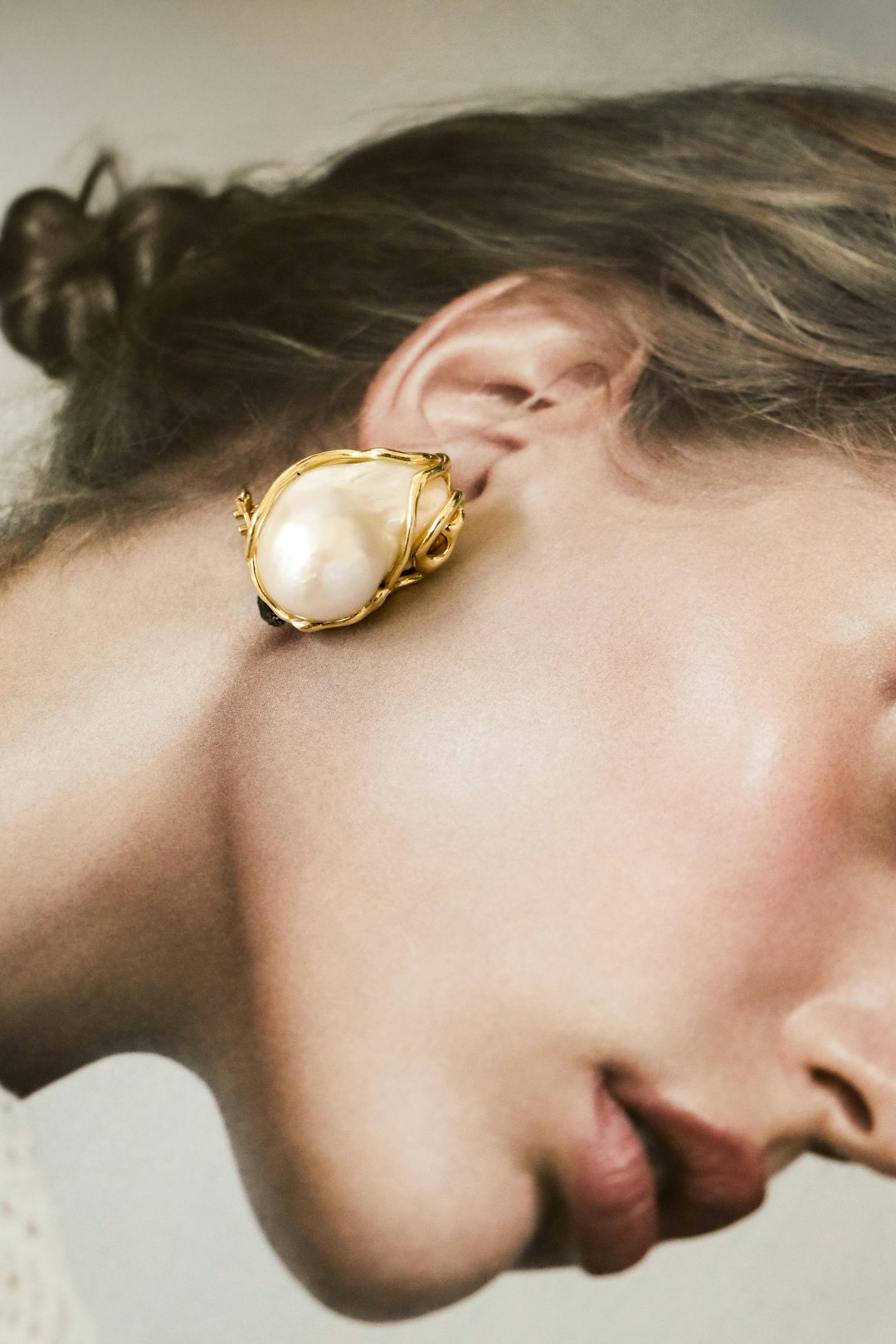 Pearl and gold earring worn on an ear, showing the pearl’s individual form