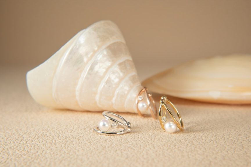 Pearl earrings resting beside a seashell on a light surface