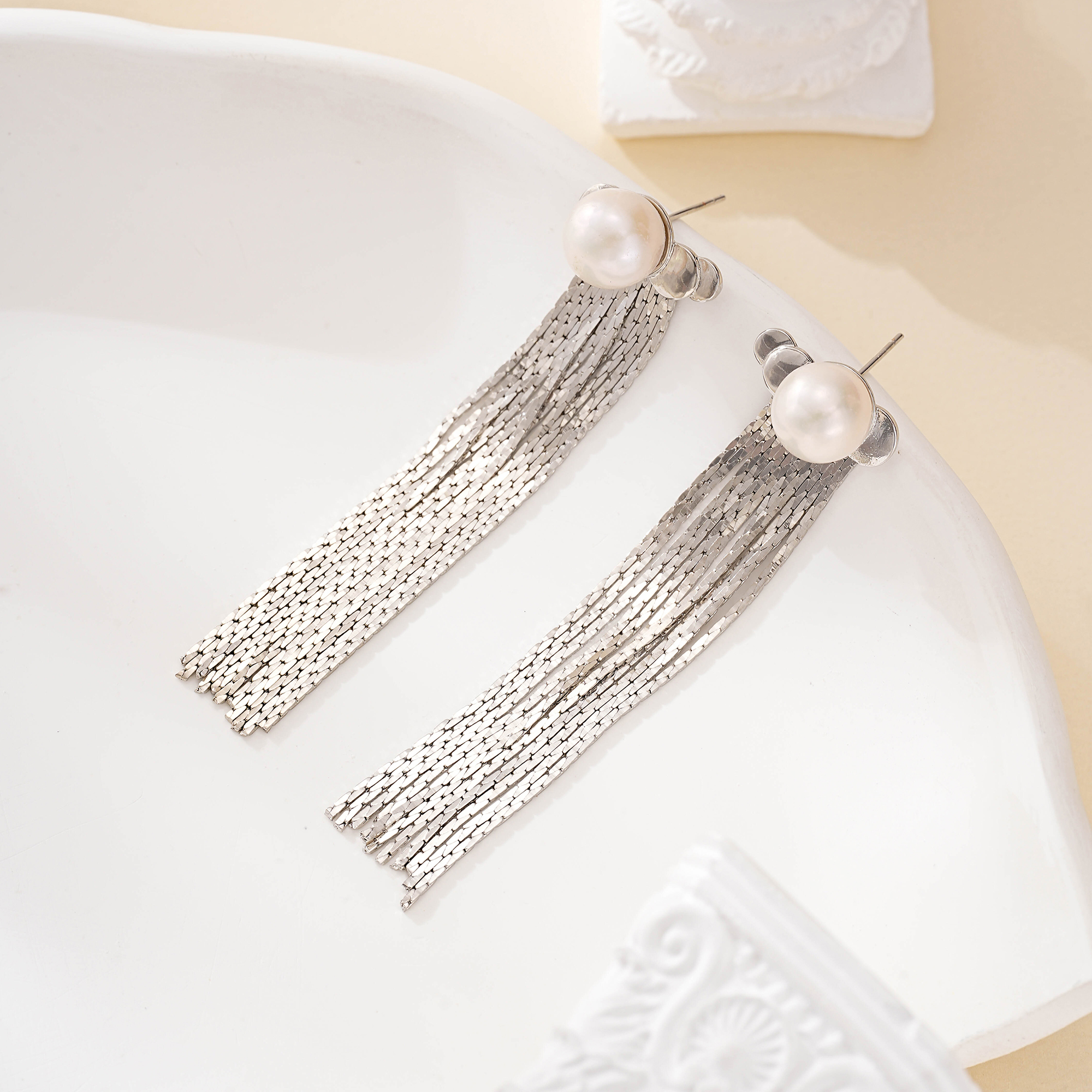 Close view of pearl stud earrings with silver-tone chain tassels