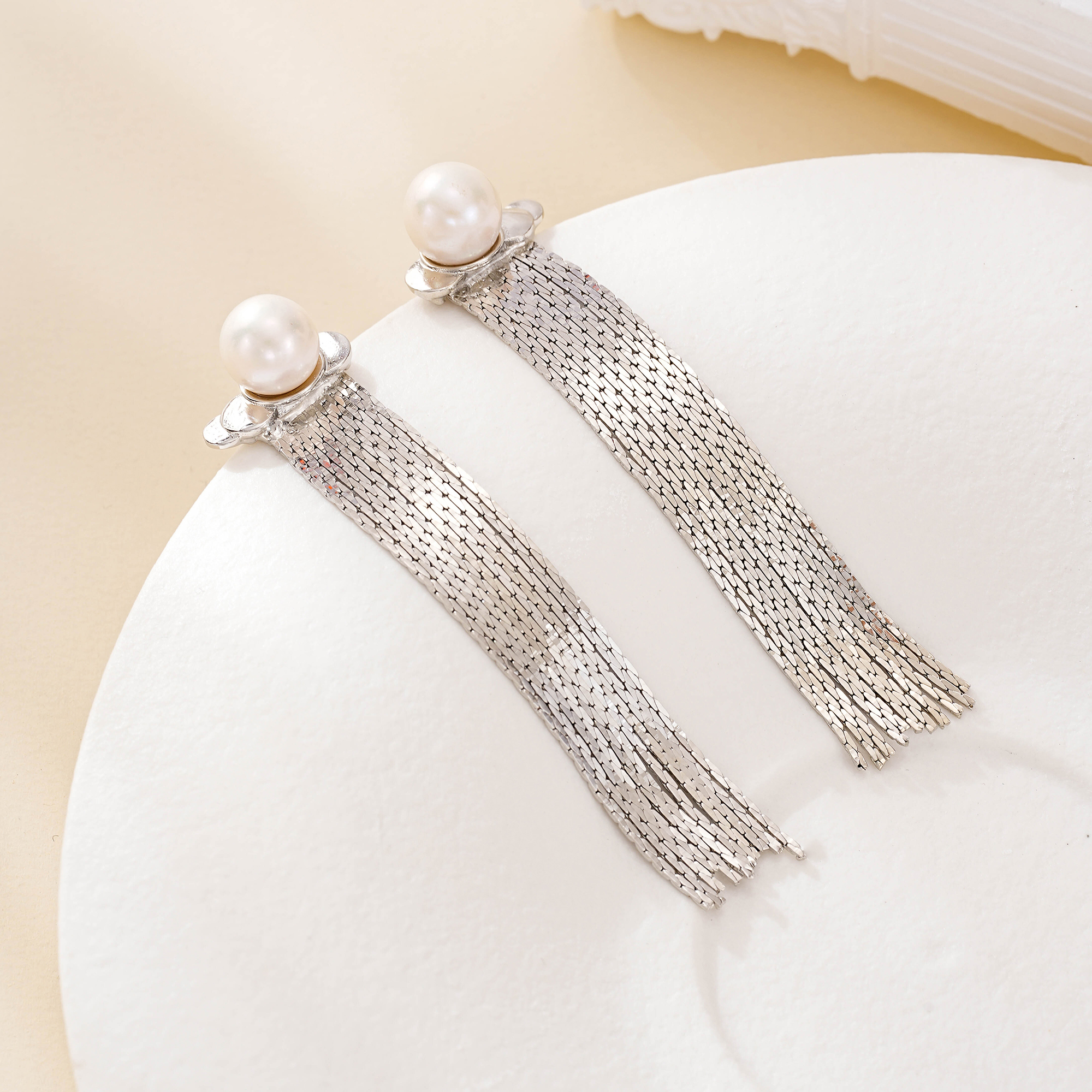 Silver-tone pearl tassel earrings displayed on a white curved surface