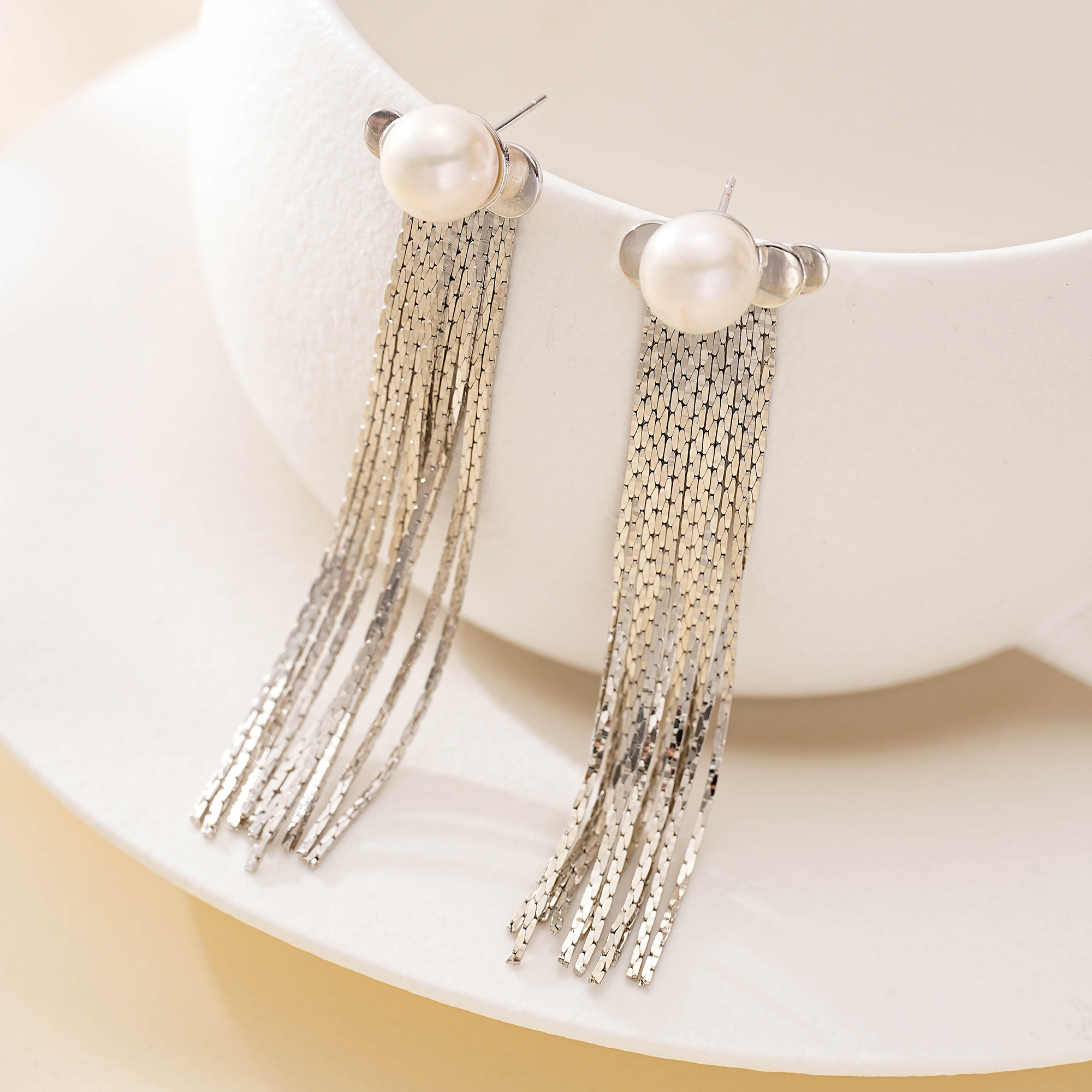 Silver-tone pearl chain tassel earrings hanging from a white display