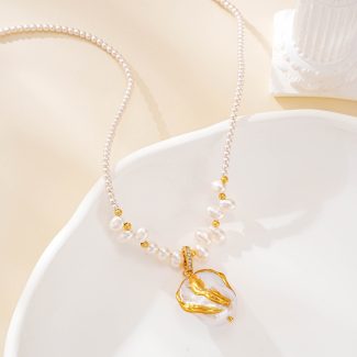 Pearl necklace with sculptural gold-tone pendant on a white dish