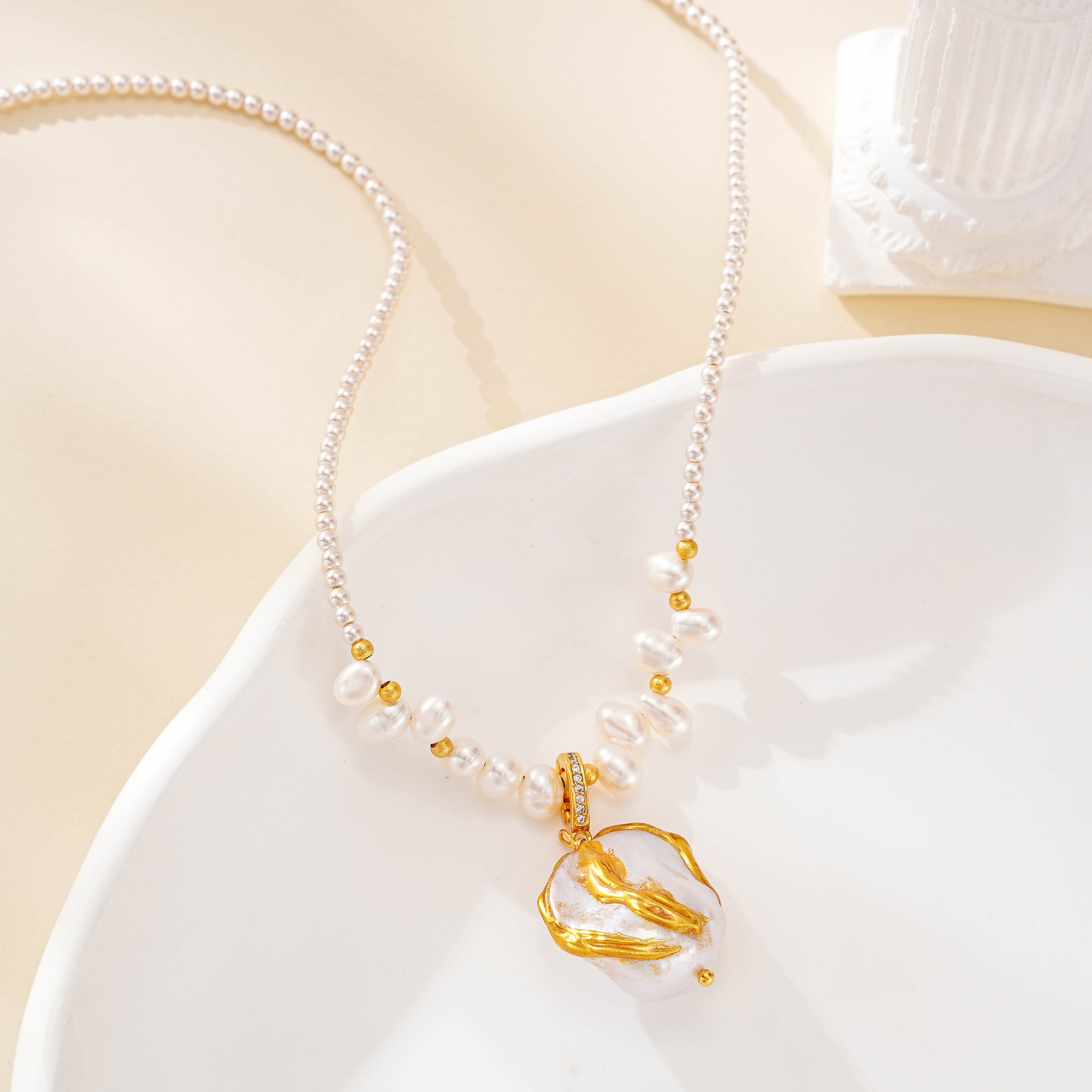 Pearl necklace with sculptural gold-tone pendant on a white dish