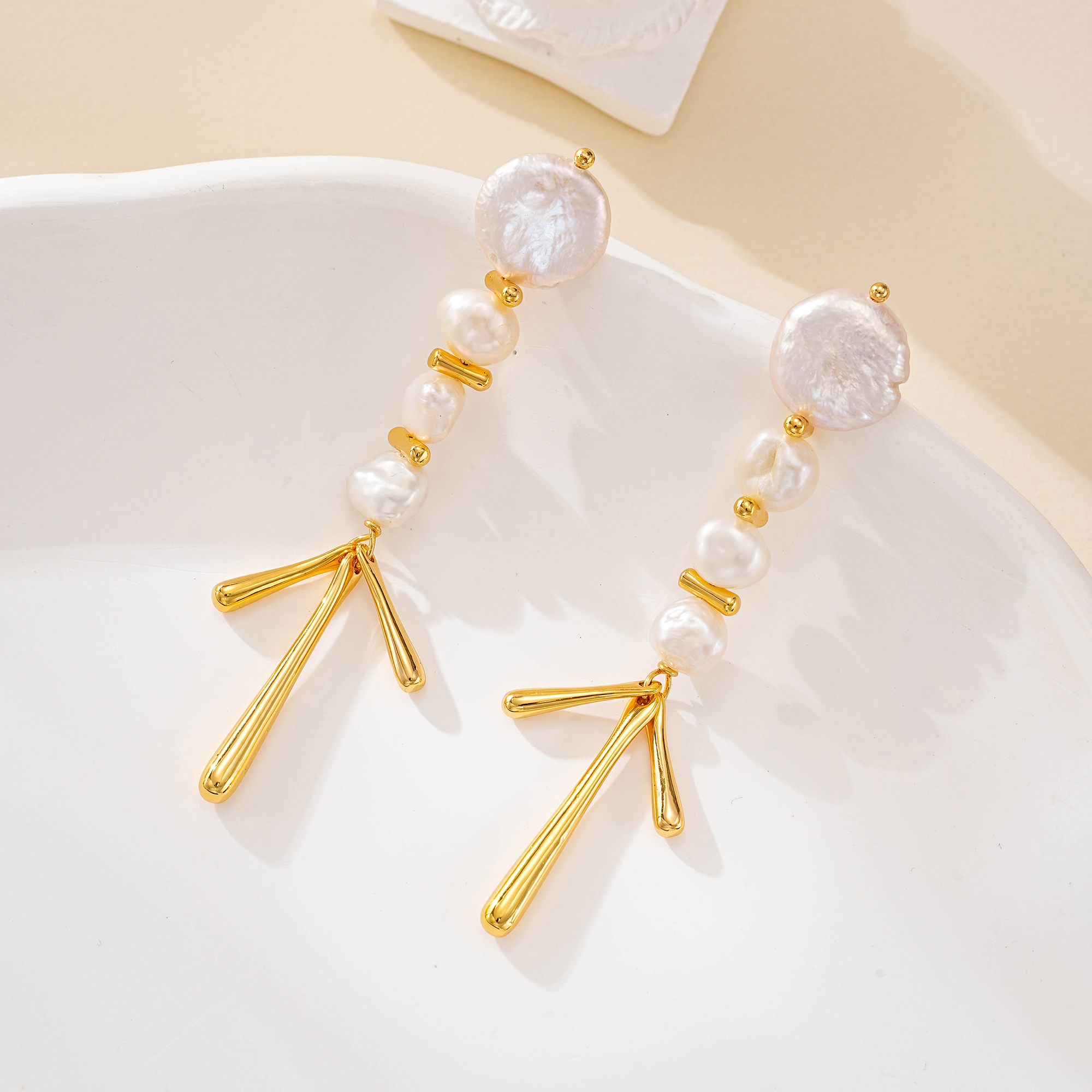 Gold-tone pearl chandelier earrings arranged on a curved white display