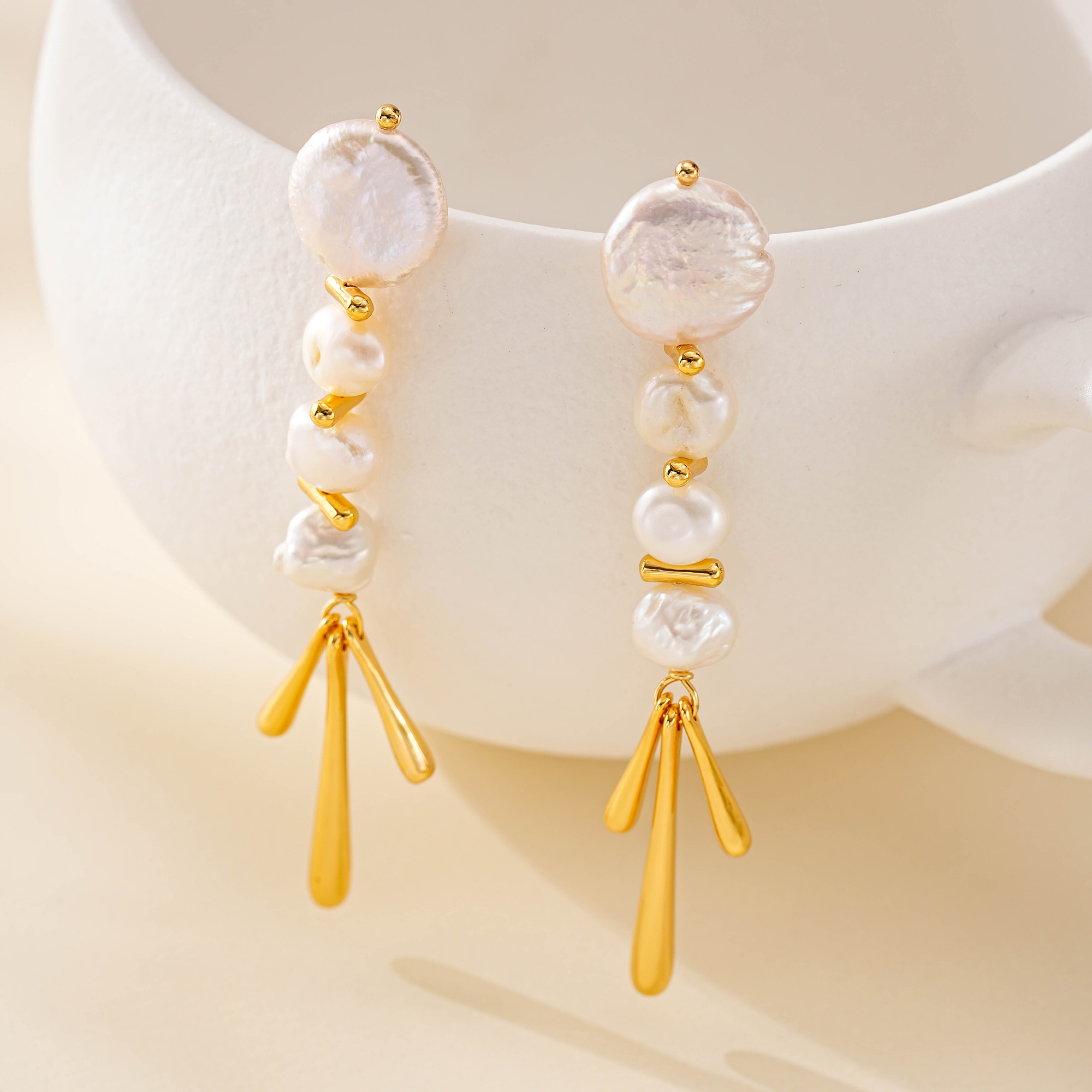 Gold-tone baroque pearl drop earrings hanging from a white display
