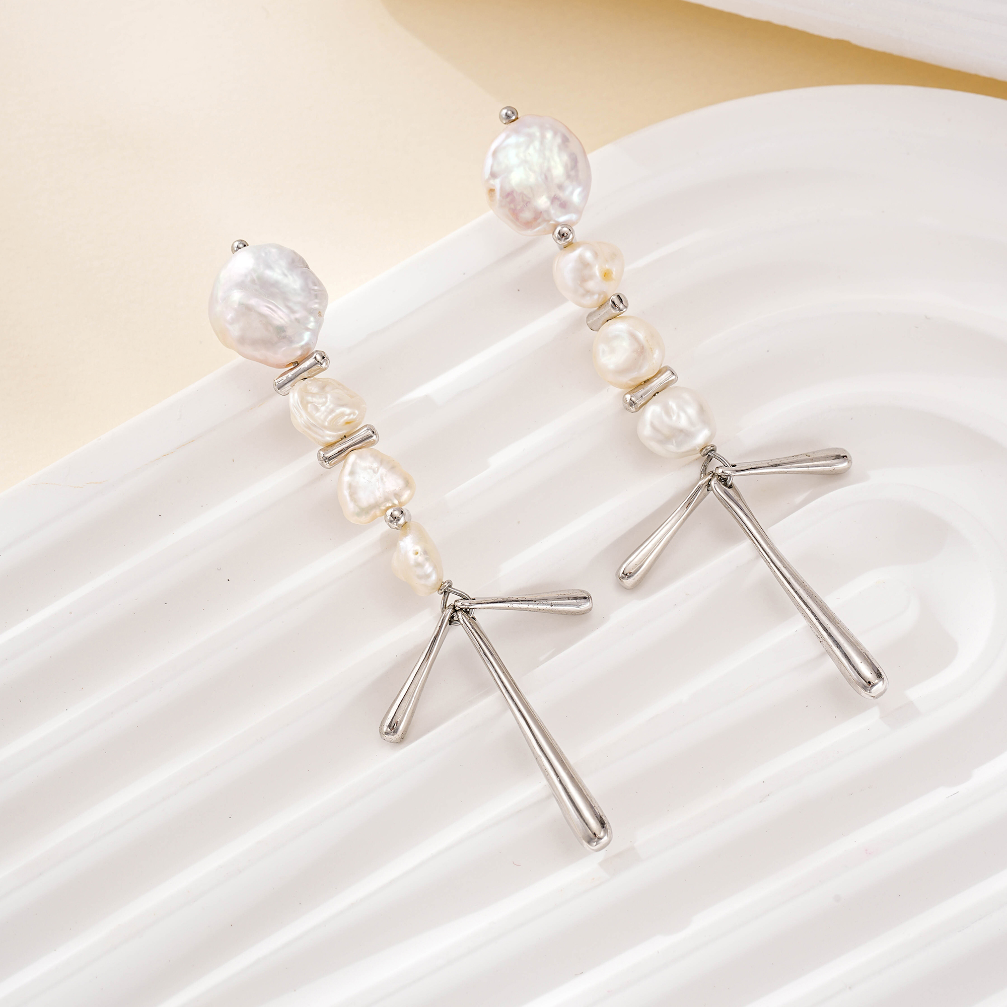 Silver-tone pearl chandelier earrings laid on a white surface