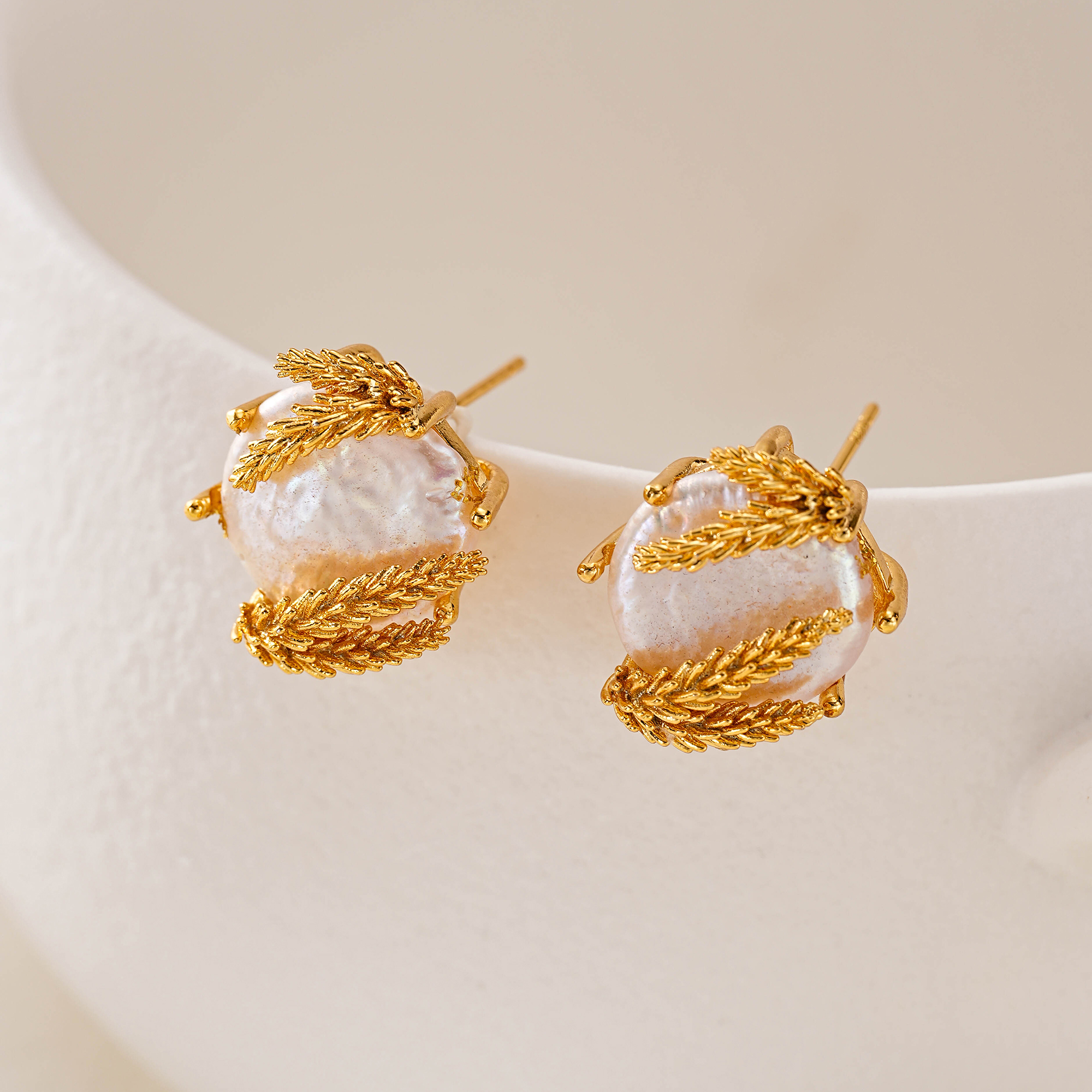 Baroque pearl studs with wheat-inspired gold-tone framing on white display
