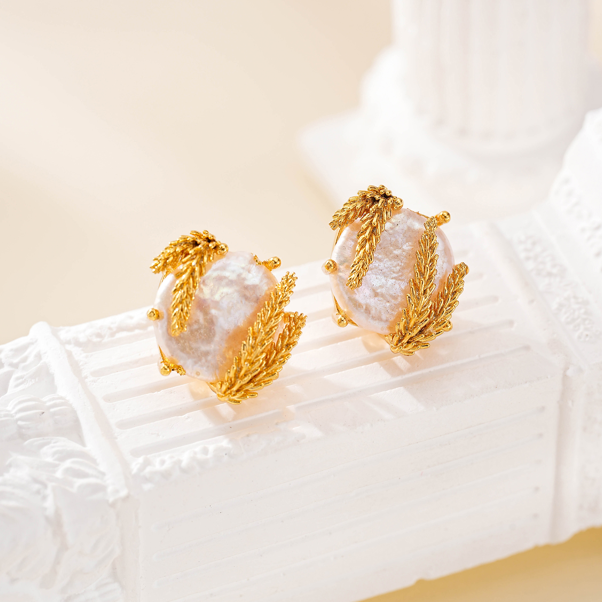 Wheat-wrapped baroque pearl studs resting on a white textured display