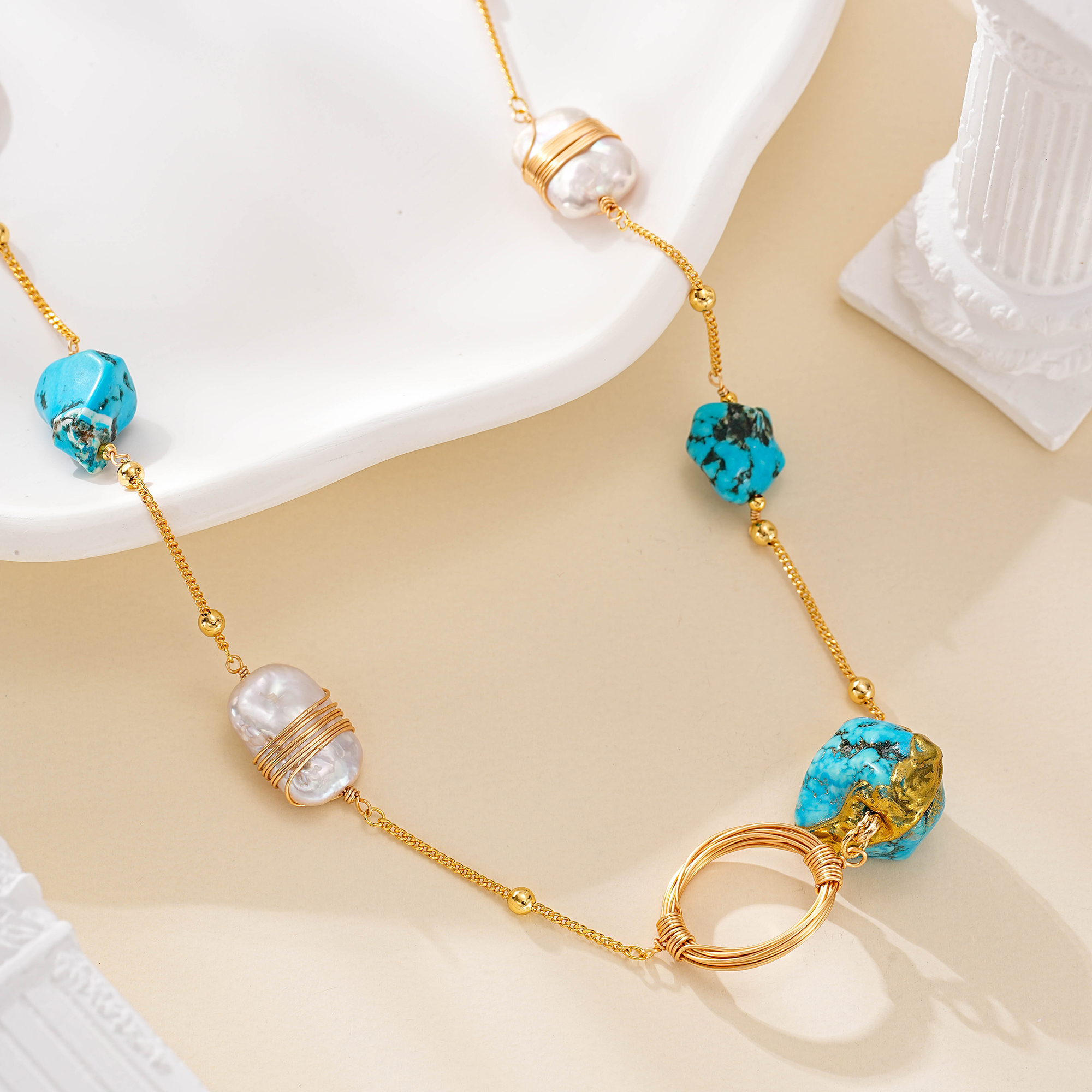 Turquoise pendant beside wire-wrapped pearls and a gold-tone ring