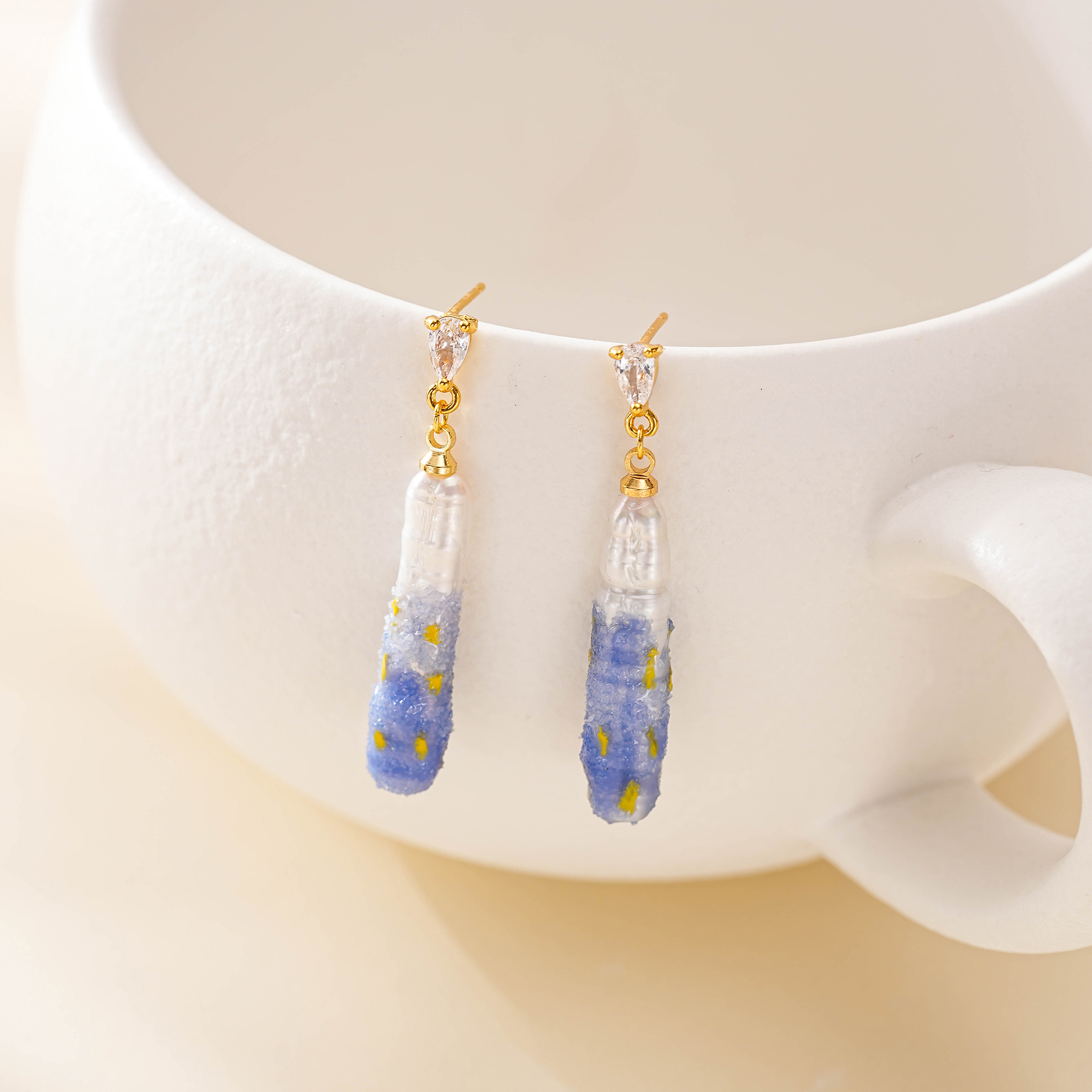 Painted pearl drop earrings hanging from a white display