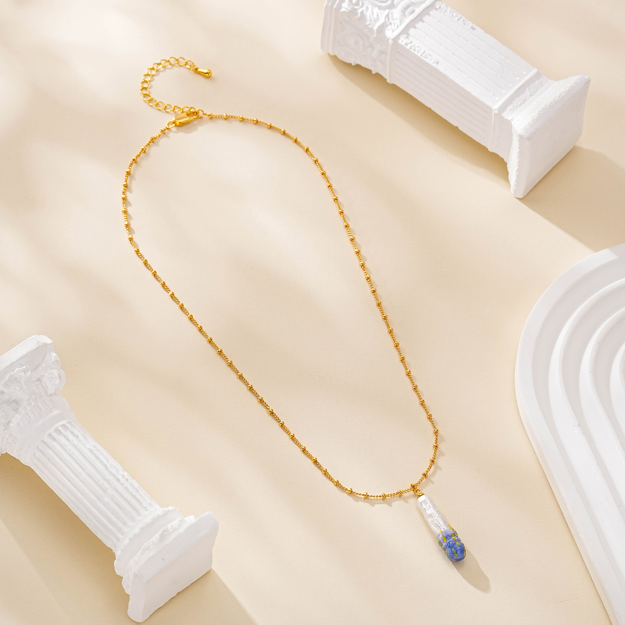 Painted pearl pendant necklace laid in a loop on a cream surface