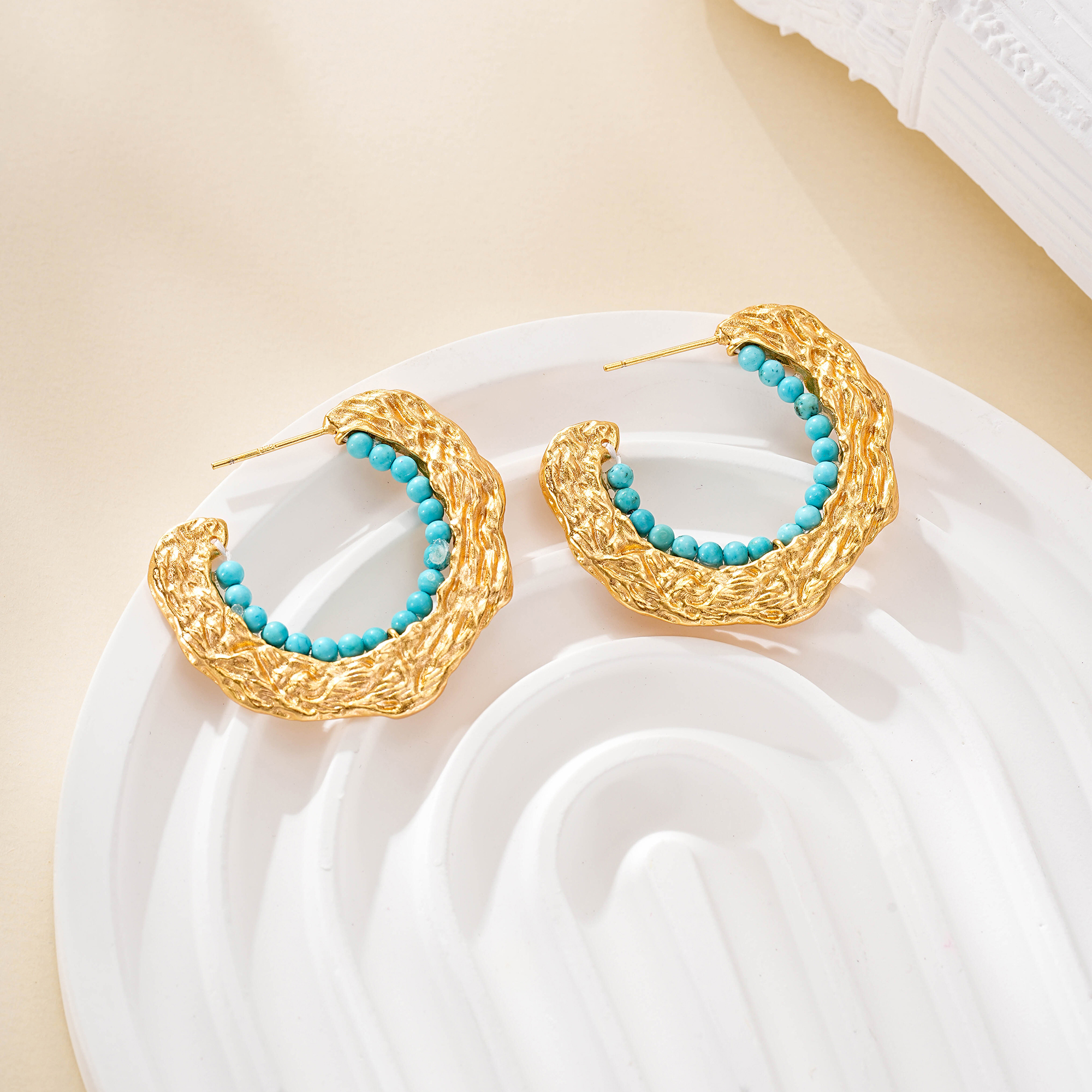 Textured C-hoop earrings with turquoise bead inner edge on a white dish