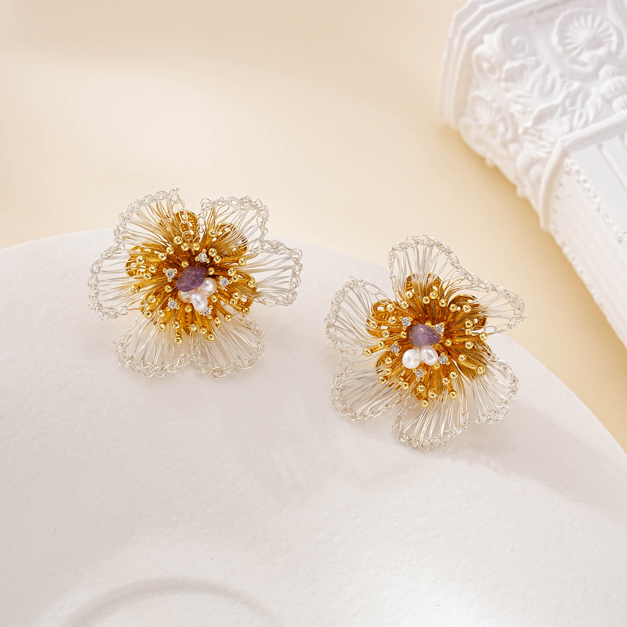 Pair of amethyst and pearl floral stud earrings on a cream surface