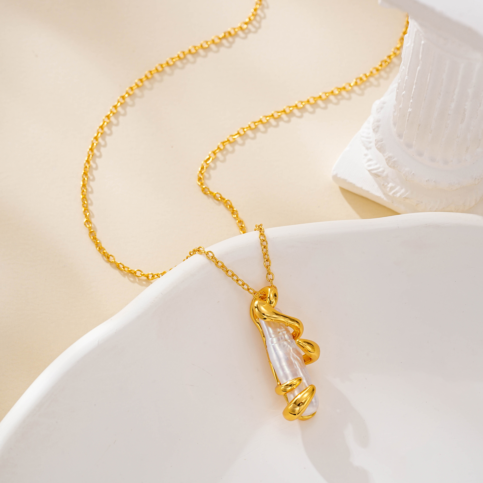Baroque pearl pendant framed by a sculptural gold-tone spiral
