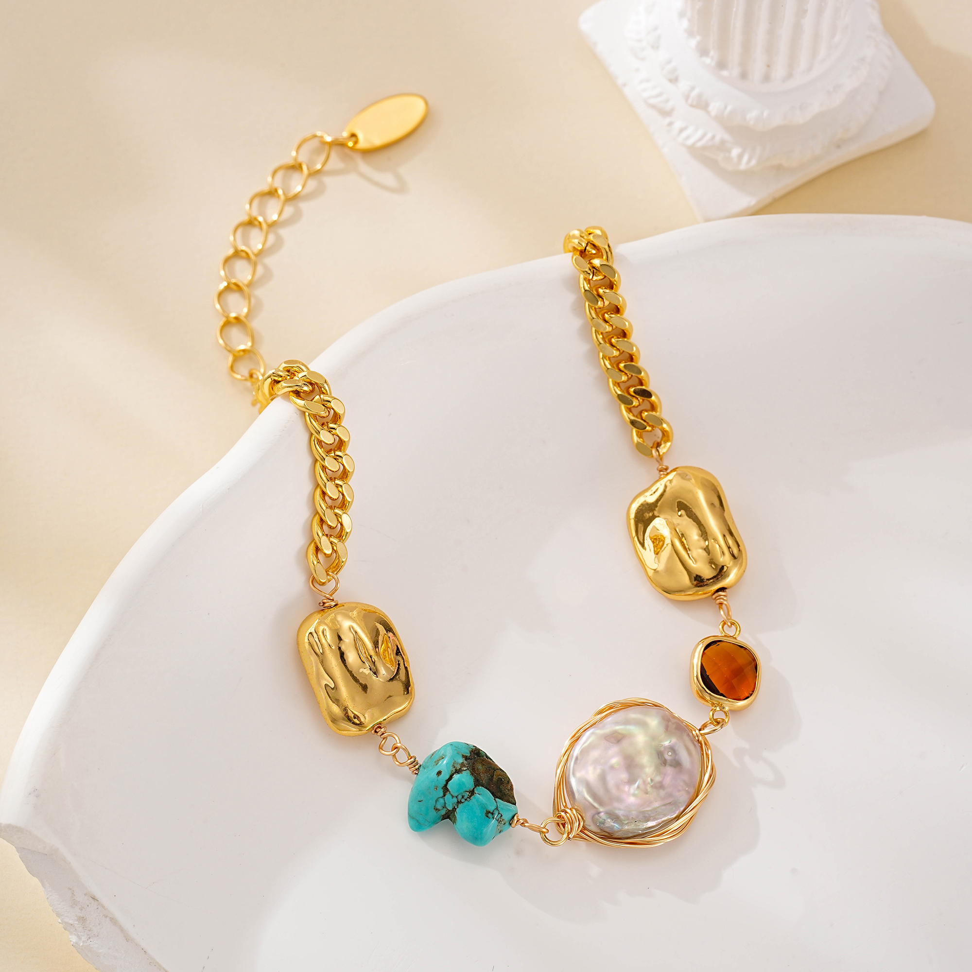 Mixed-link bracelet draped over a white dish, showing pearl and red accent