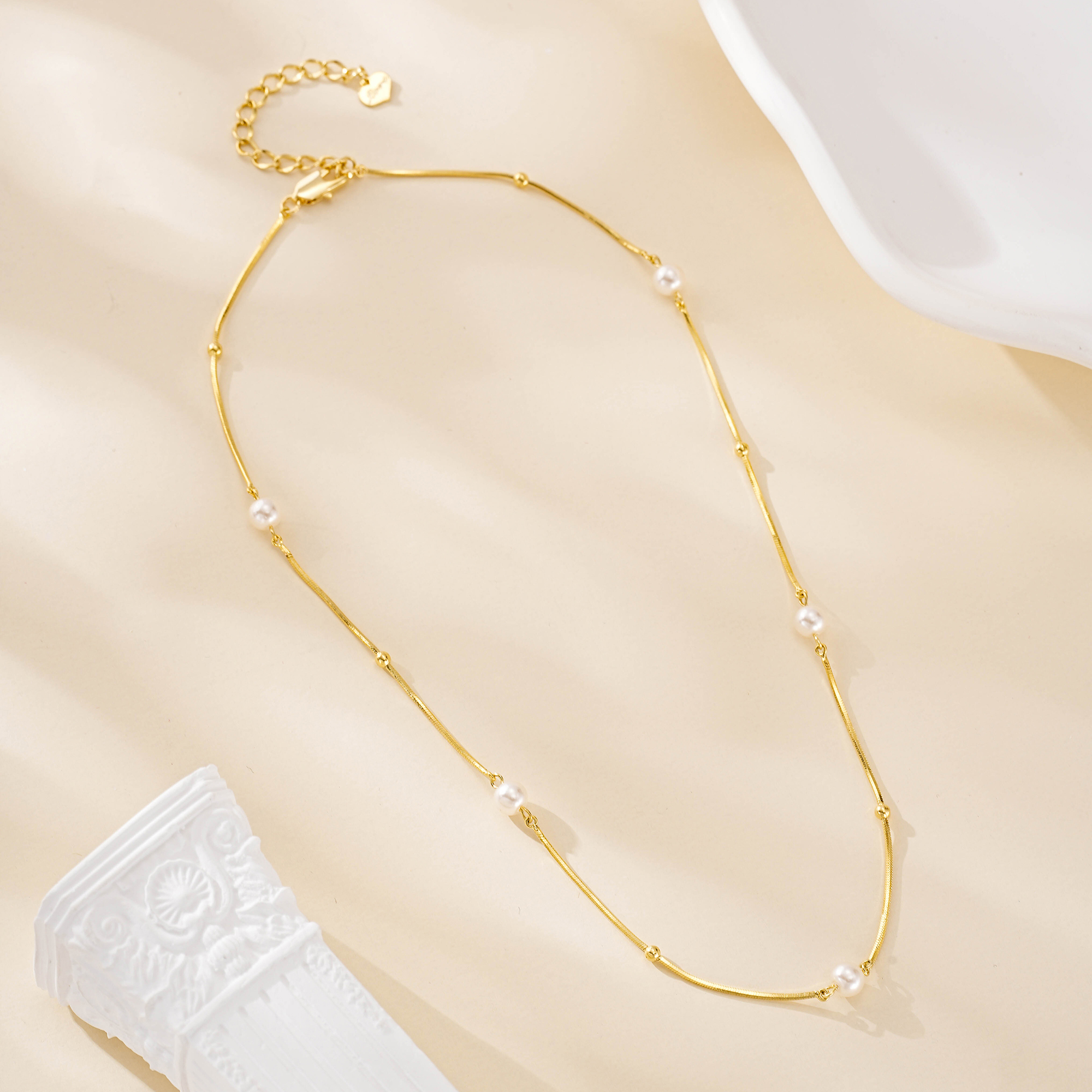 Short pearl necklace laid out to show its gold-tone extender chain