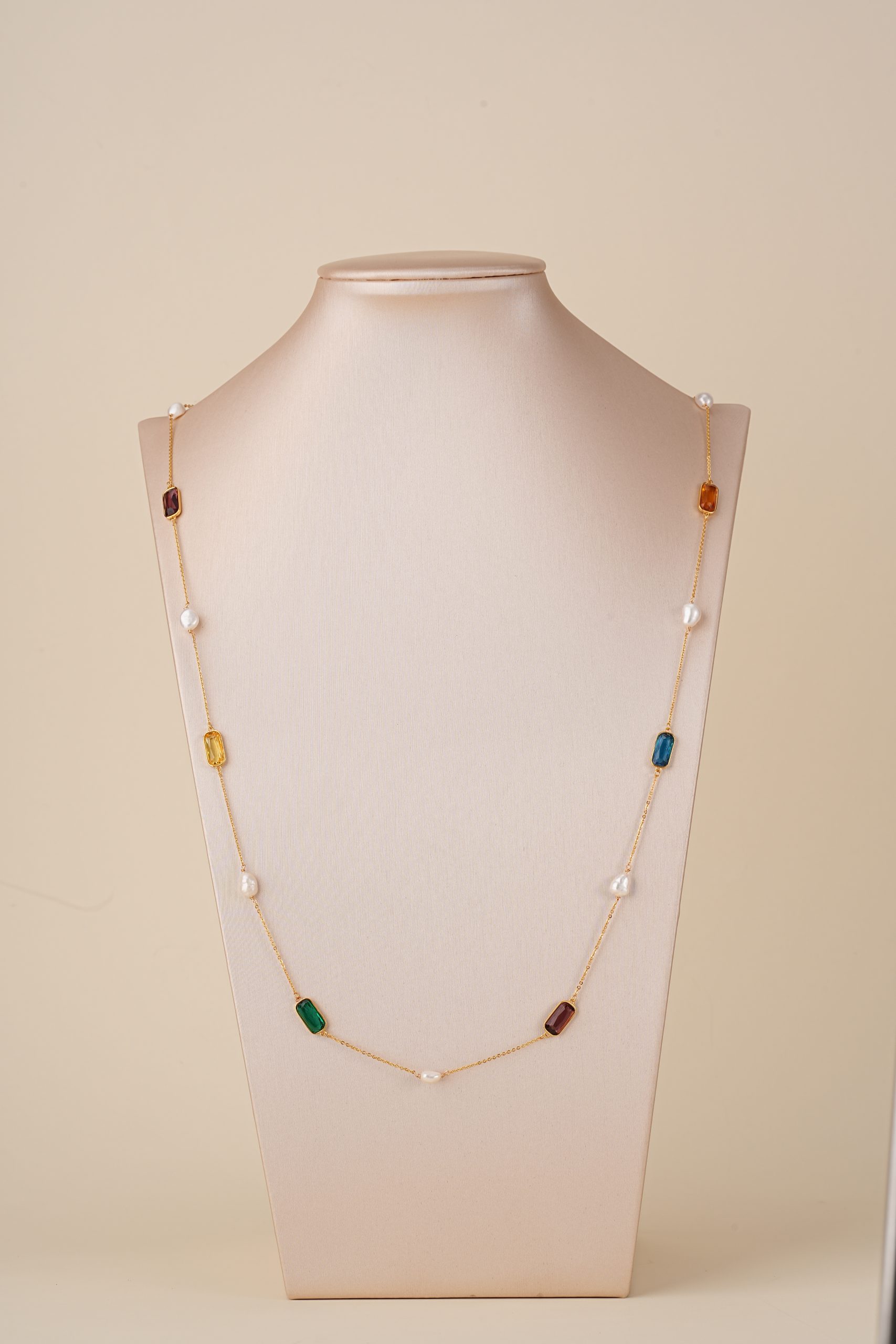Long multicolor gemstone and pearl necklace displayed on a bust