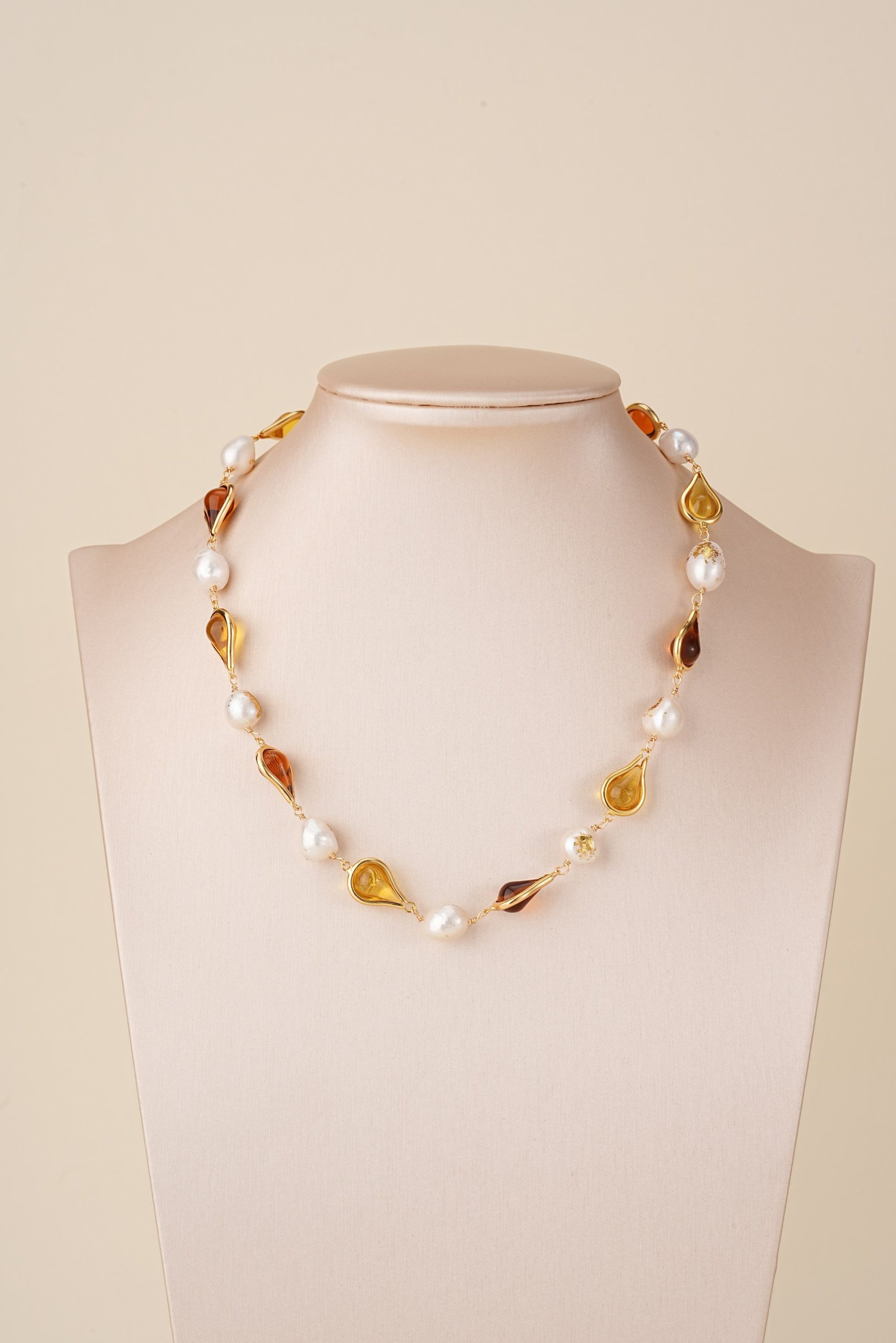 Amber-toned resin and pearl necklace displayed on a bust