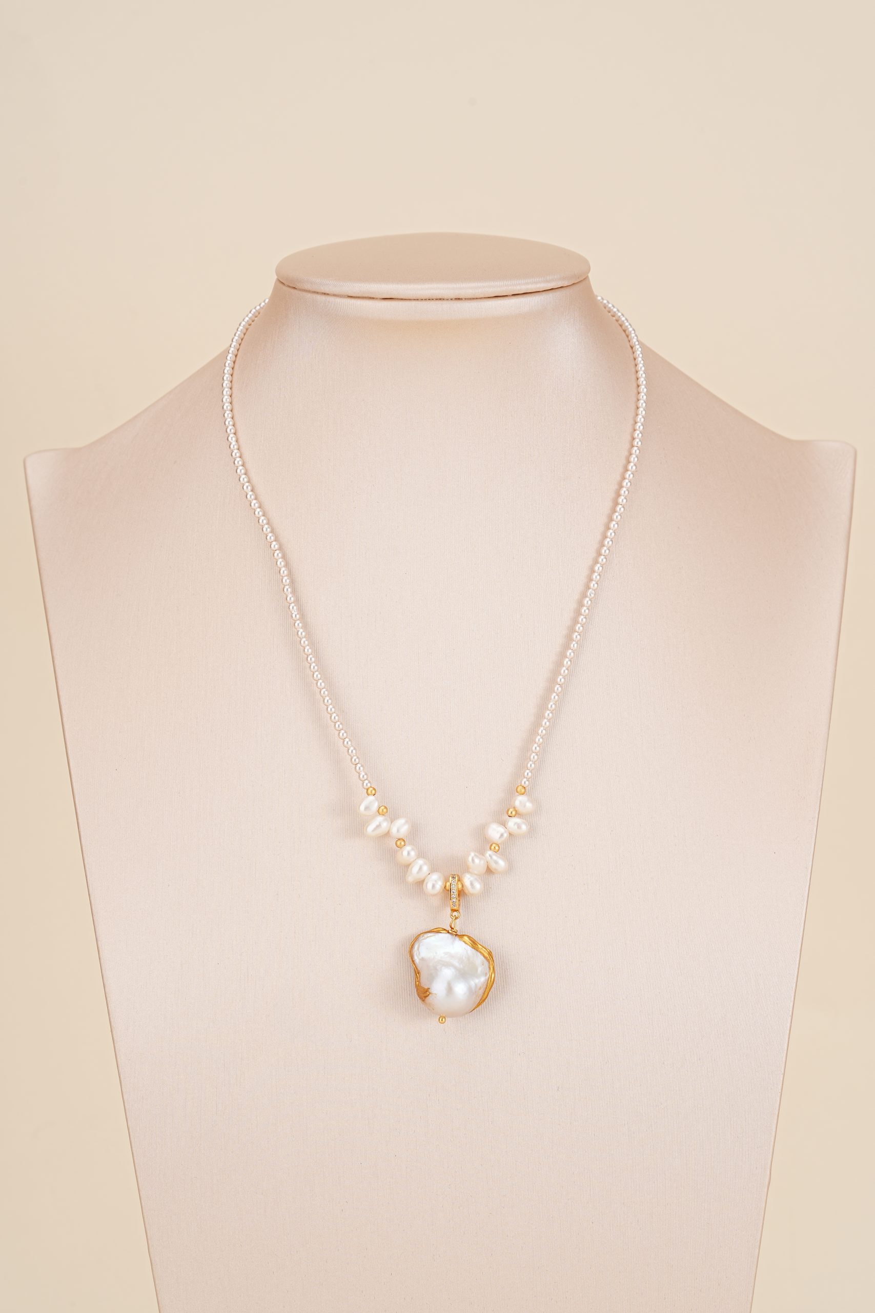 Pearl-accented necklace with white pendant displayed on a bust