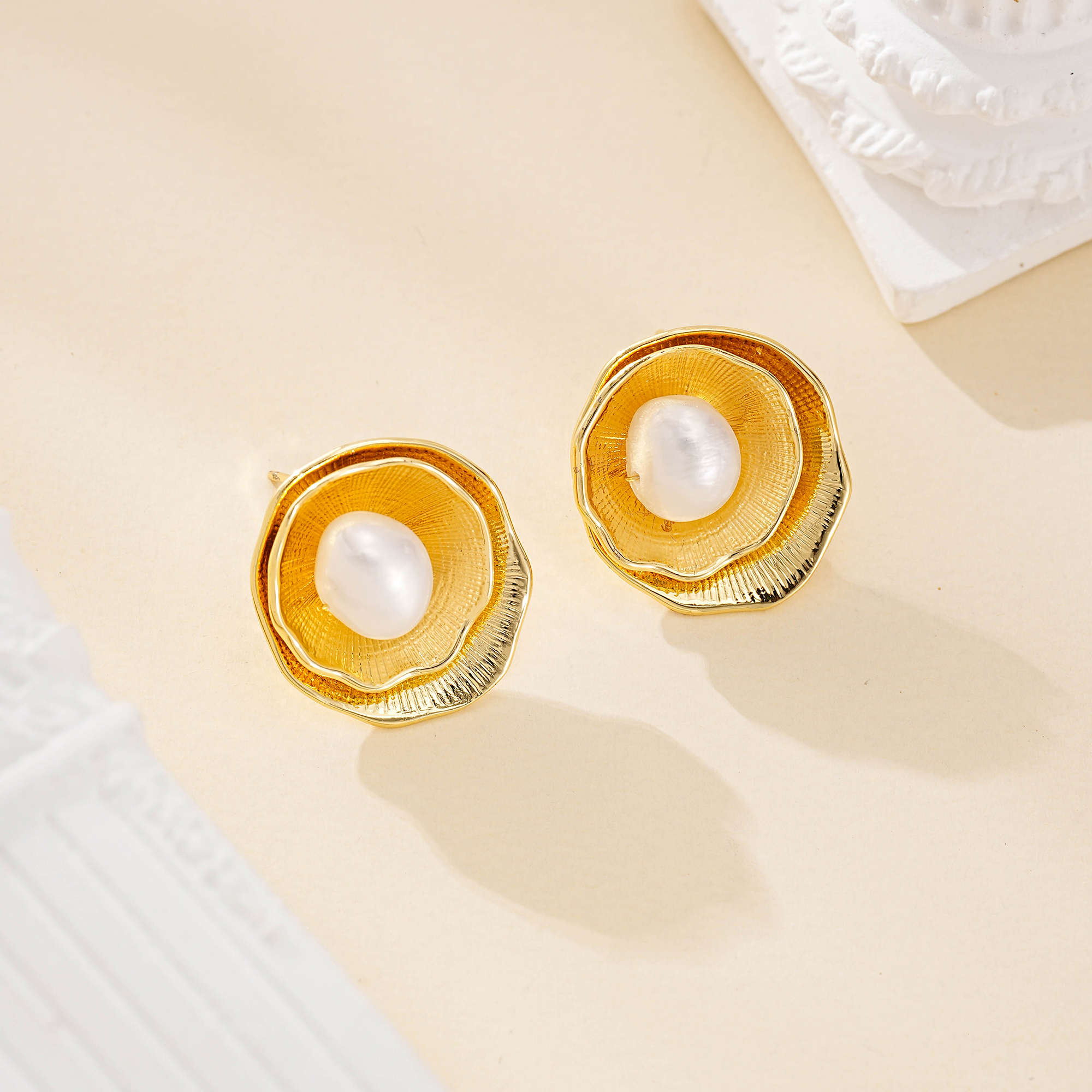 Angled view of round floral pearl studs on a cream backdrop