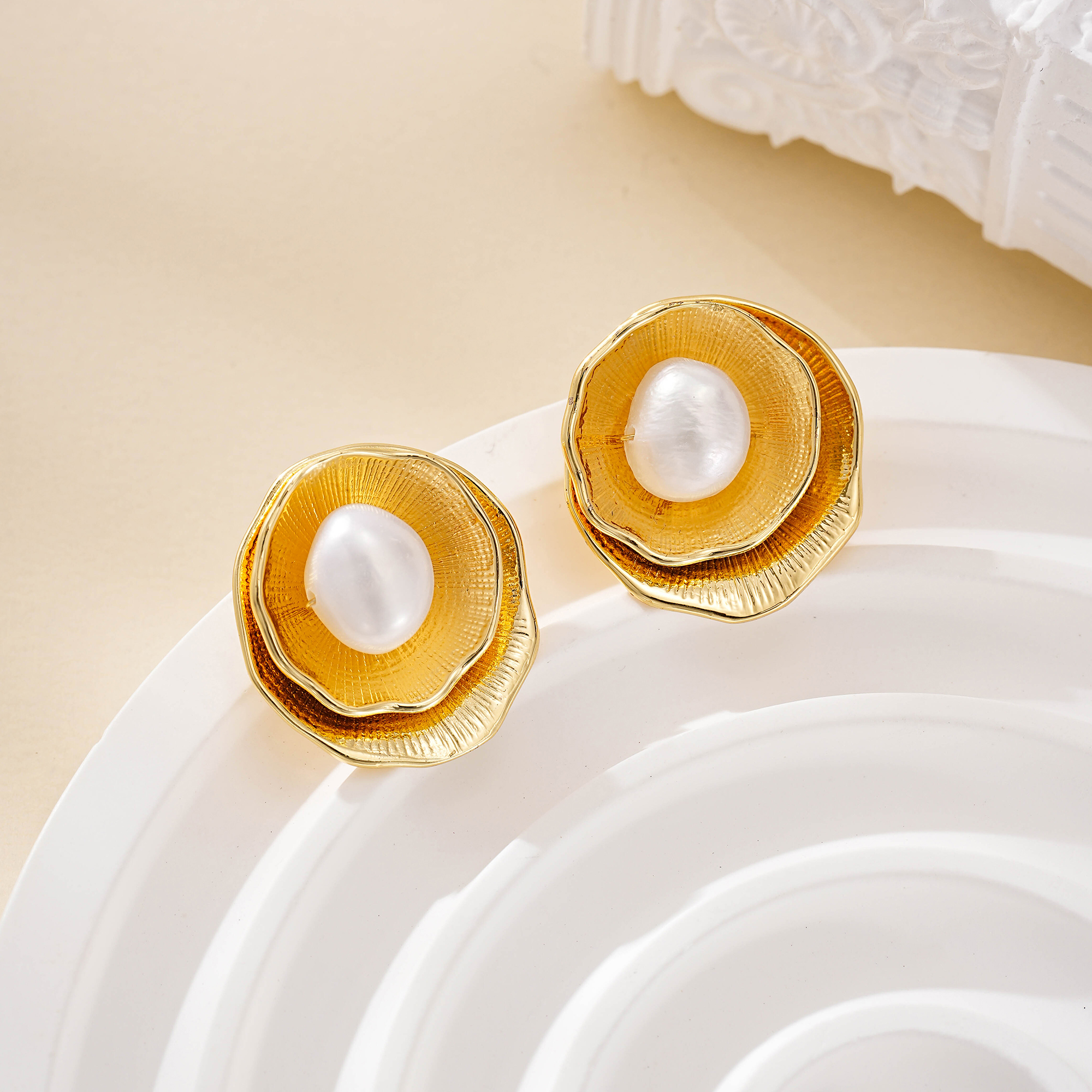 Pair of layered petal pearl earrings on a white ceramic dish