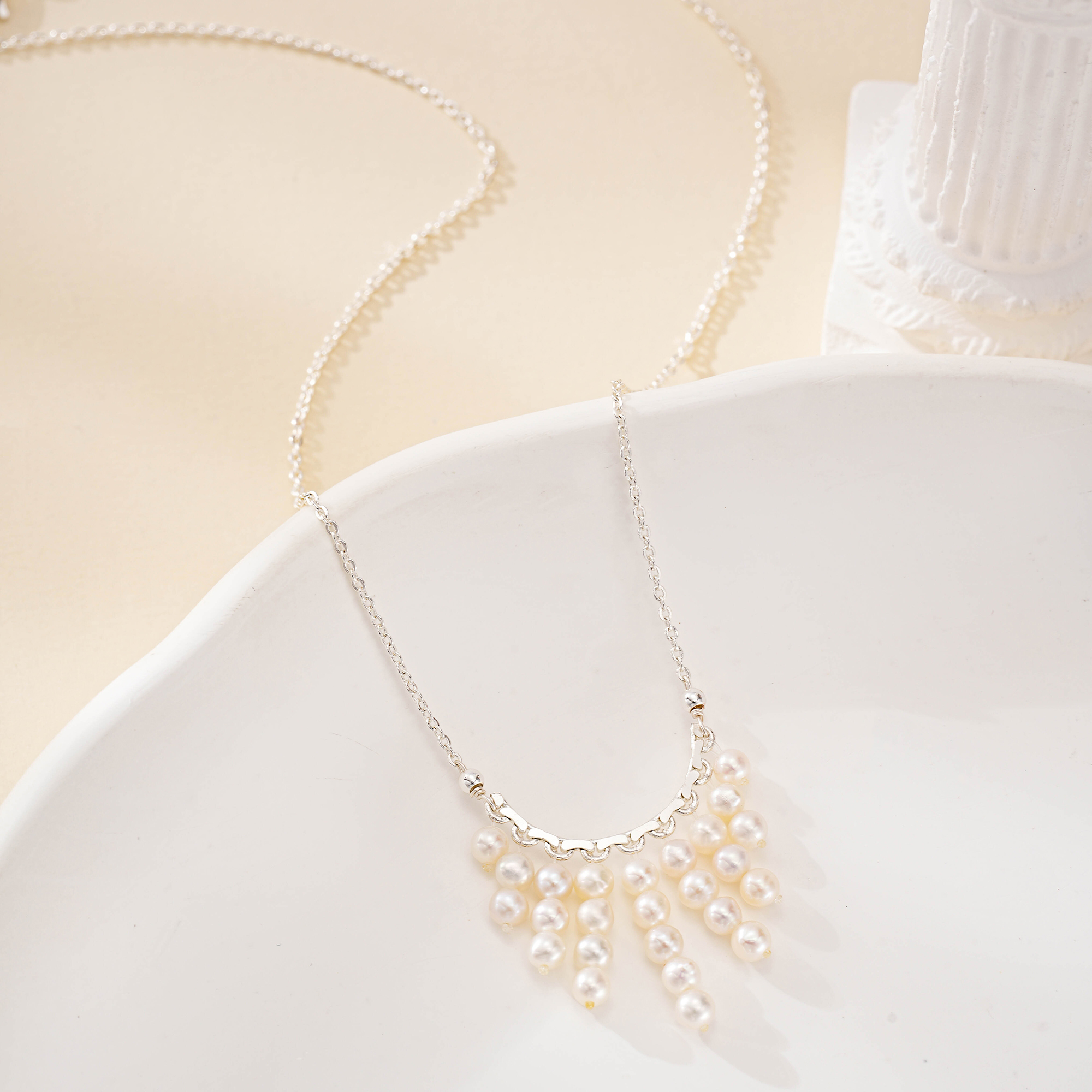 Pearl fringe necklace arranged across a pale ceramic dish