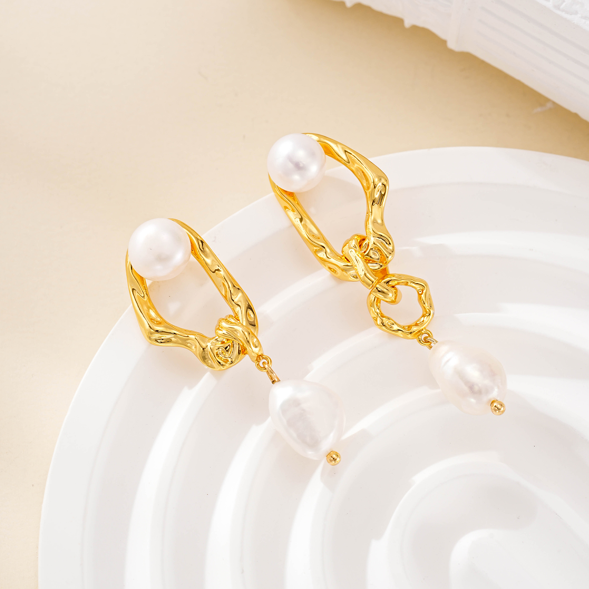 Pair of asymmetric pearl earrings on a white ceramic dish