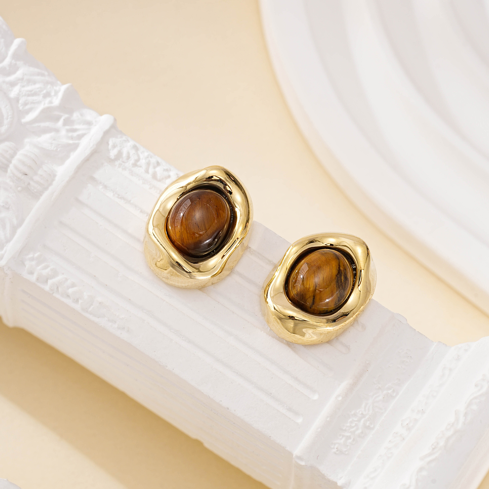 Angled view of oval tiger eye earrings on a white decorative surface