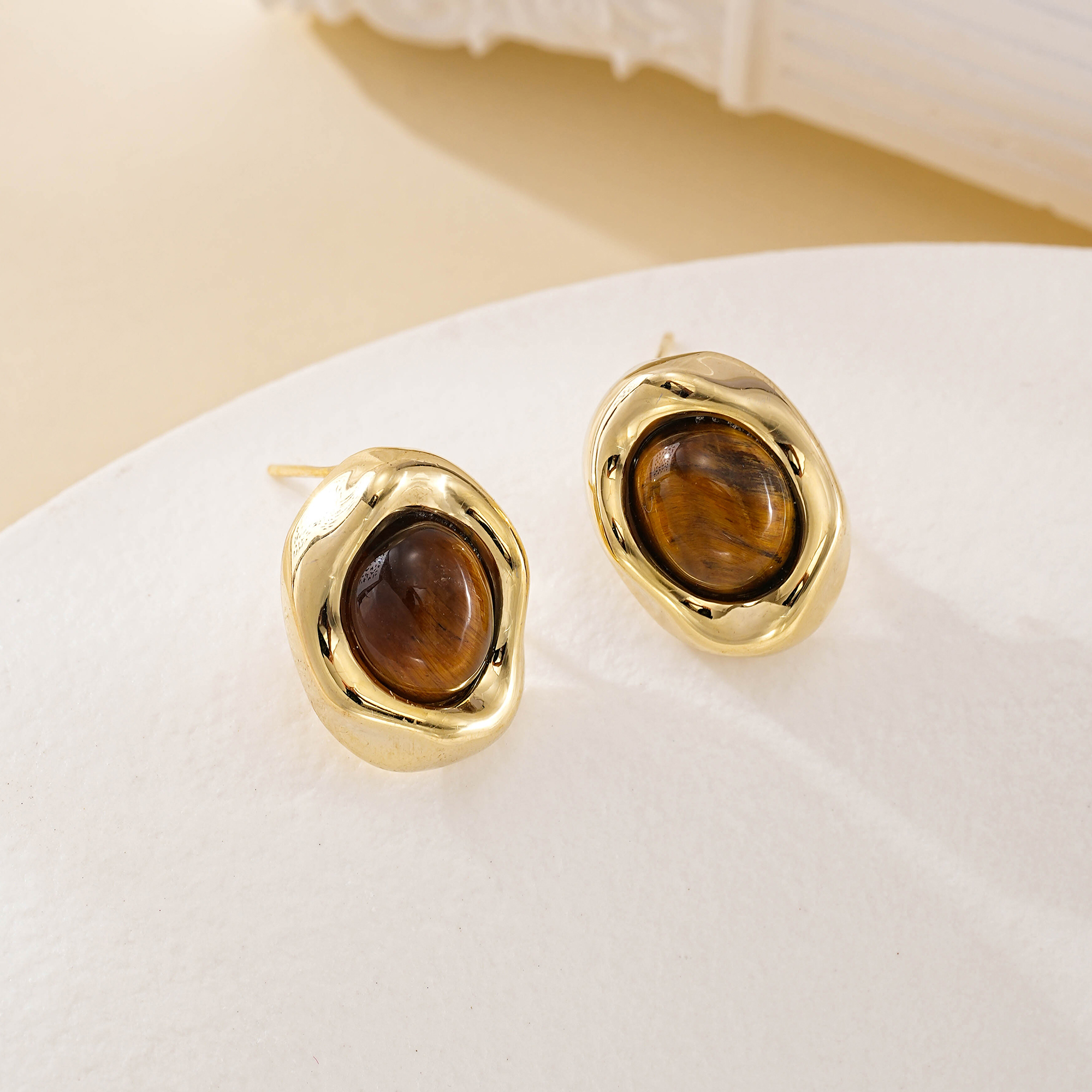 Pair of gold-toned tiger eye studs resting on a cream dish