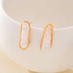 Pair of elongated baroque pearl earrings against a white ceramic dish
