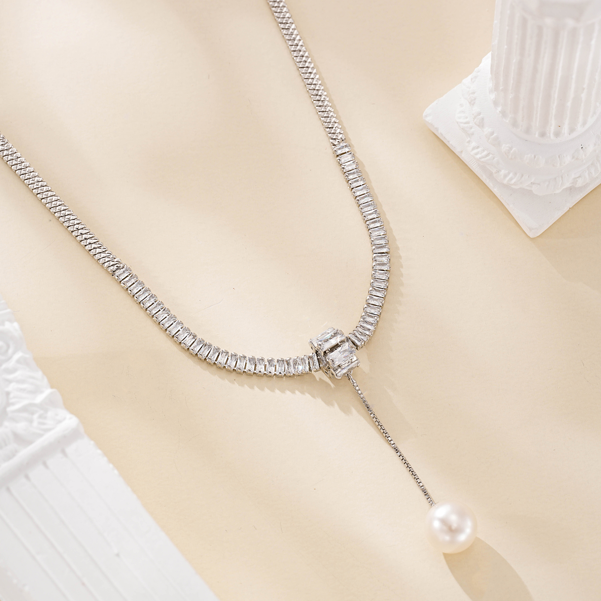 Close view of silver-tone chain and clear accents above a round freshwater pearl drop