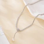 Silver-tone snake chain necklace with a long pearl drop draped beside a white dish