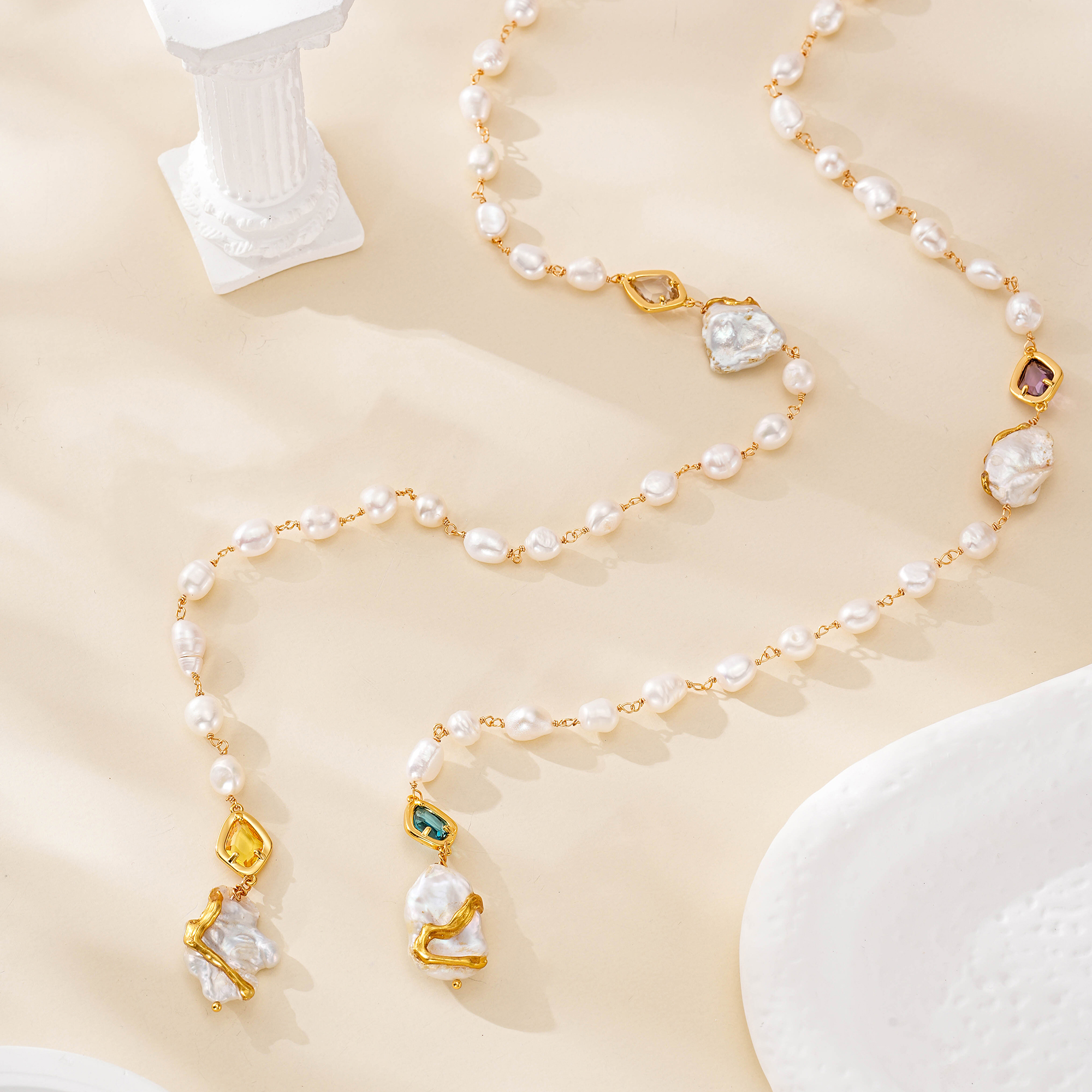 Extra-long pearl necklace draped across a cream backdrop with colored accents