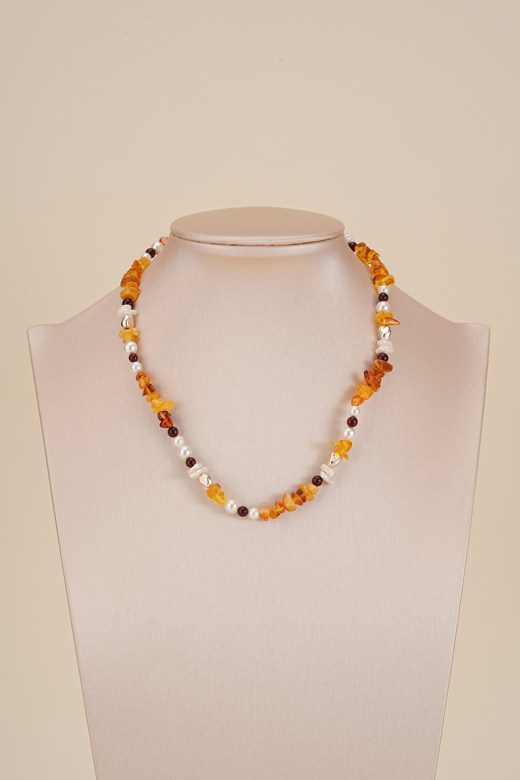 Amber-toned gemstone and baroque pearl necklace on a neutral bust