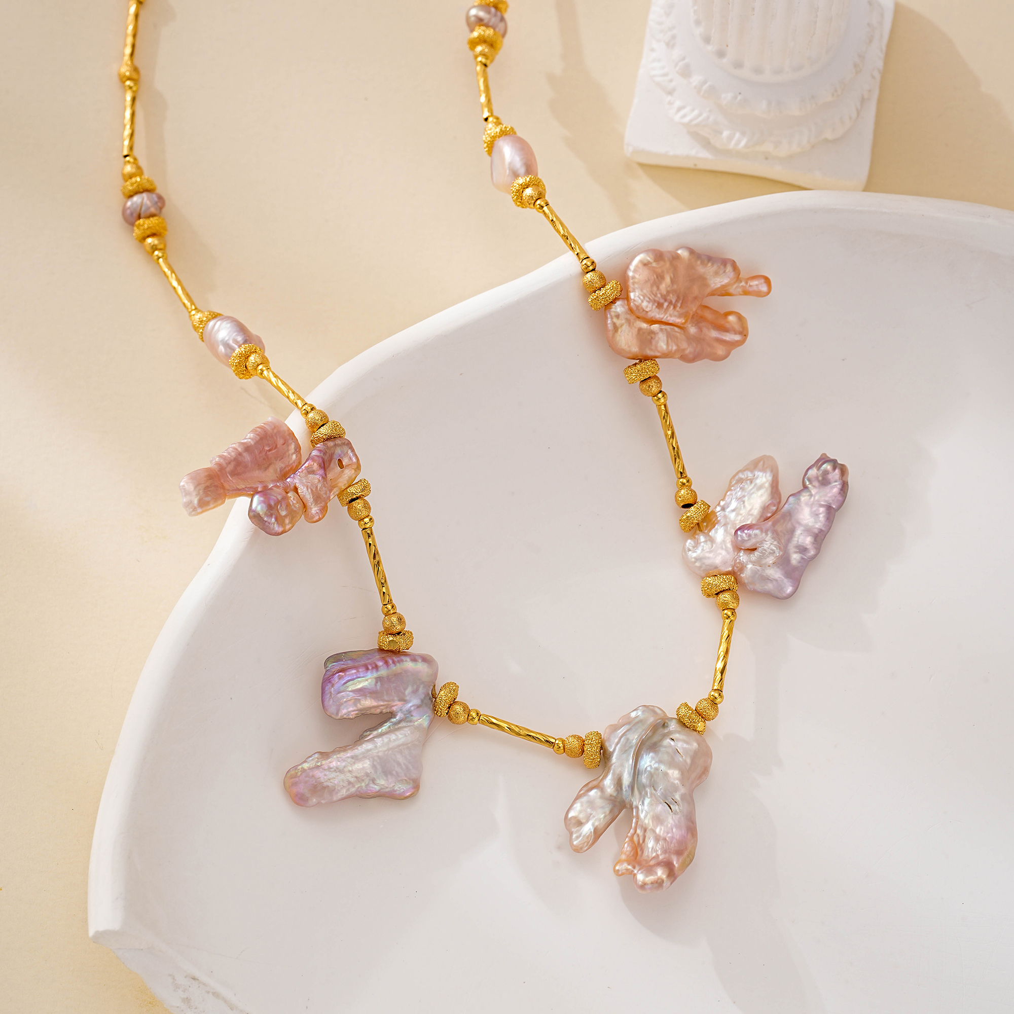 Close-up of irregular pink baroque pearls hanging above a pale dish