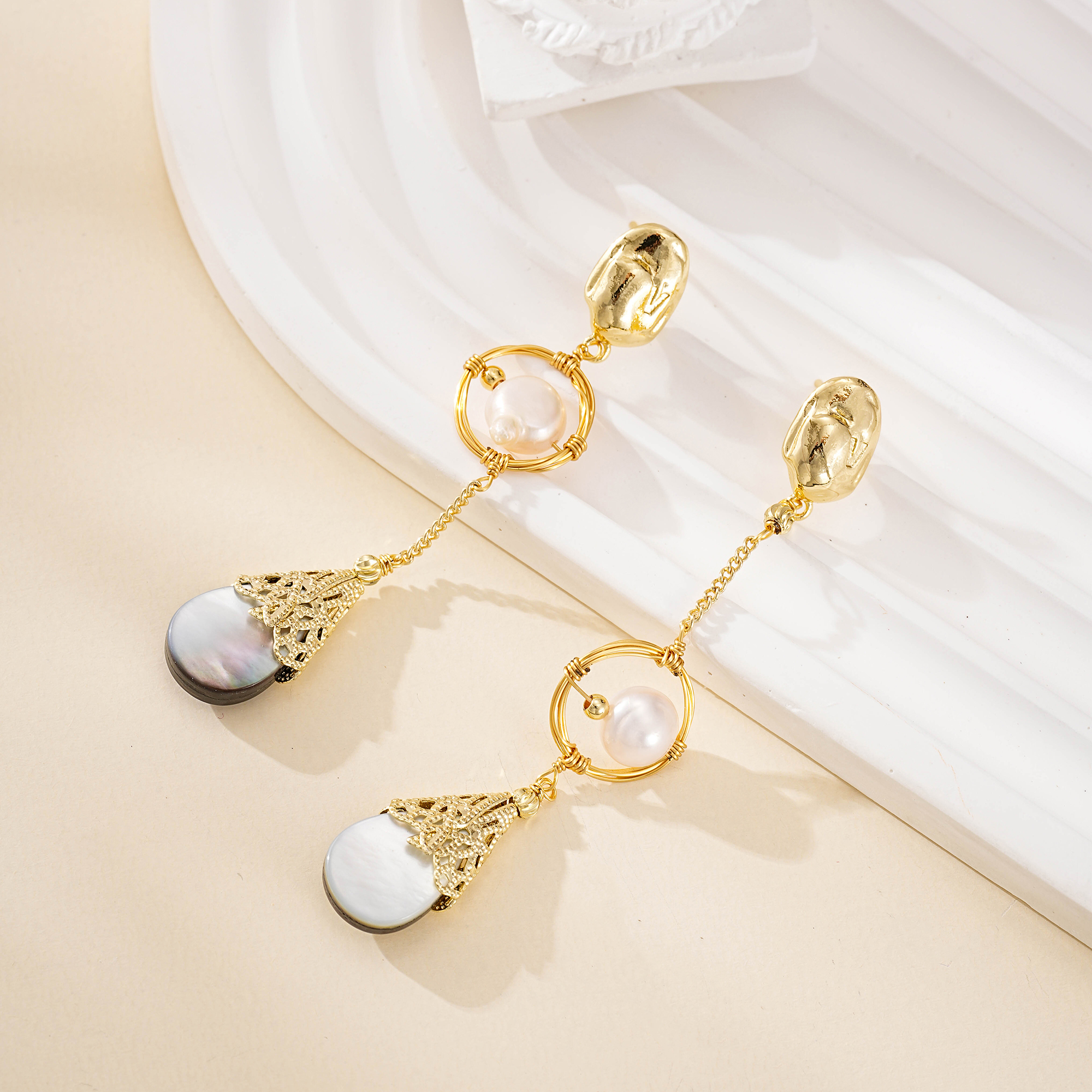 Dark teardrop shell pendants below sculptural pearl earrings