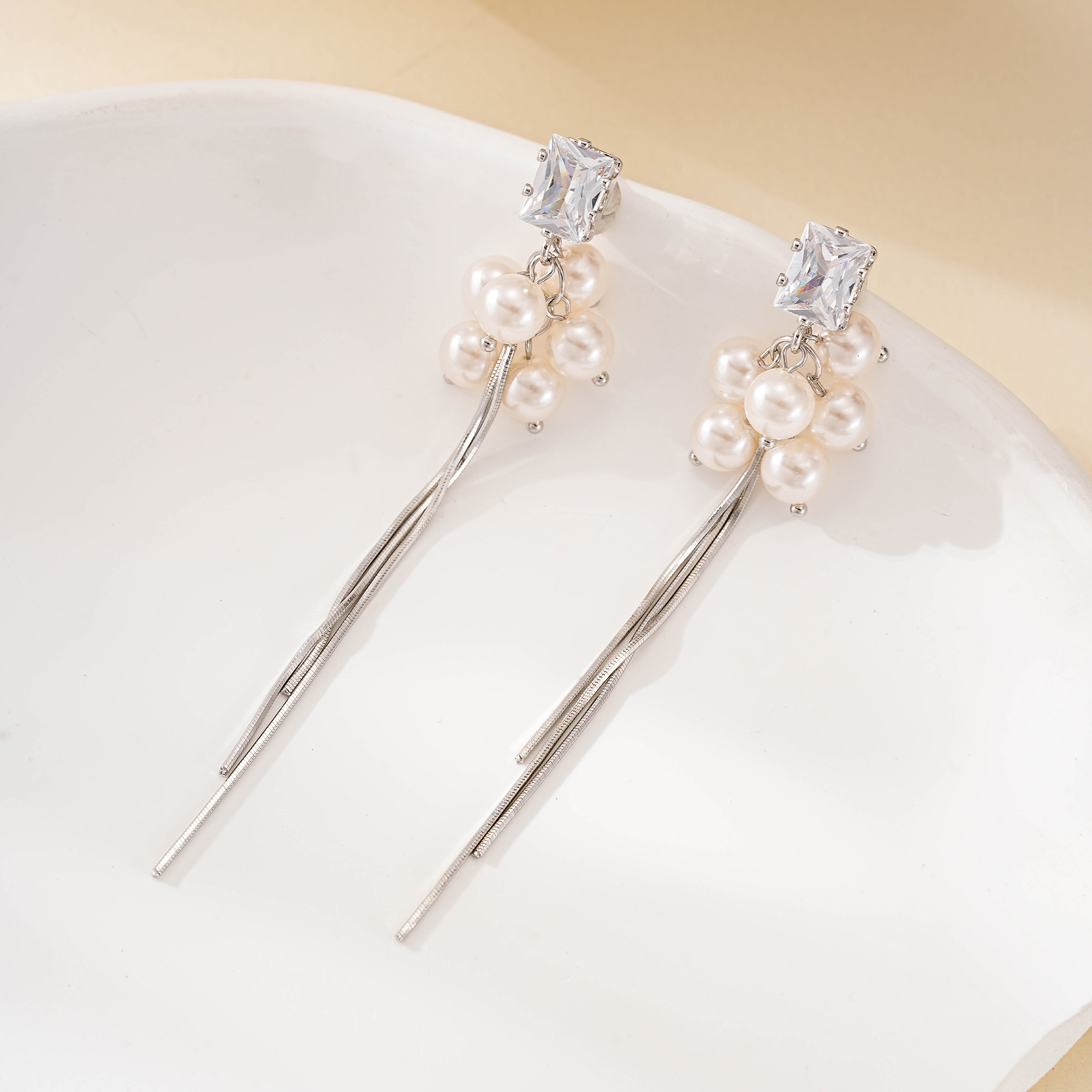 Rectangular clear-stone studs above pearls and silver tassels
