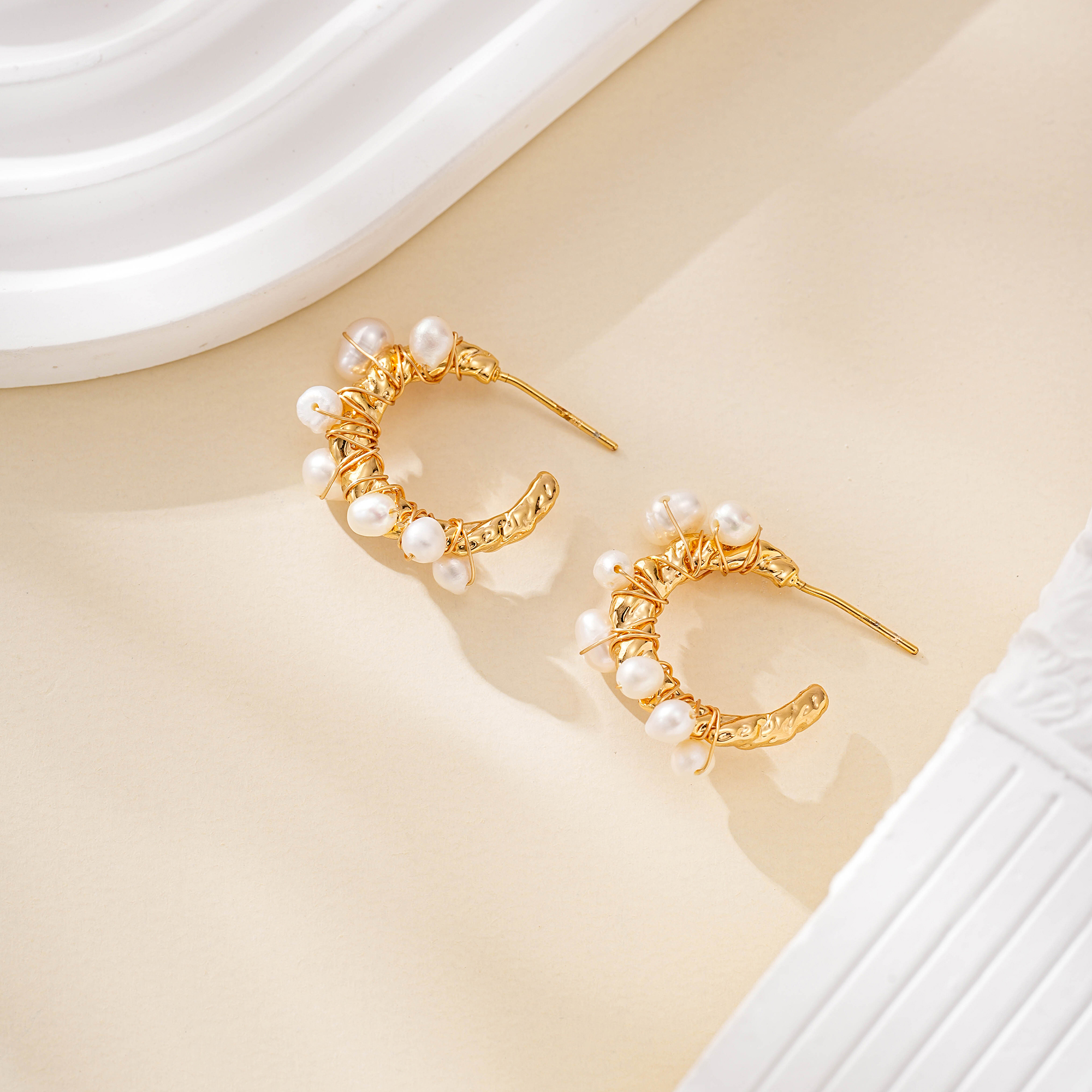 Pair of pearl-wrapped open hoop earrings on cream surface